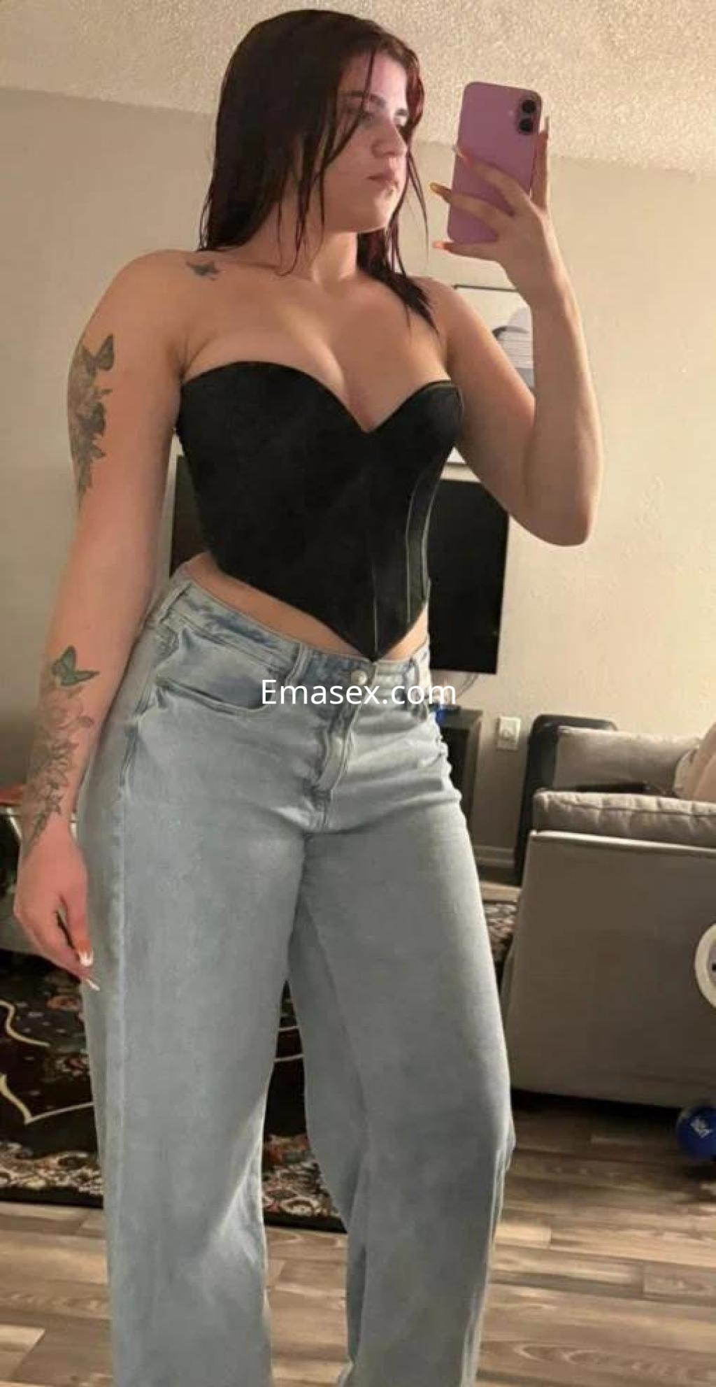 La puta en Tarragona lleva un corsé negro y jeans claros, mostrando su figura frente al espejo.