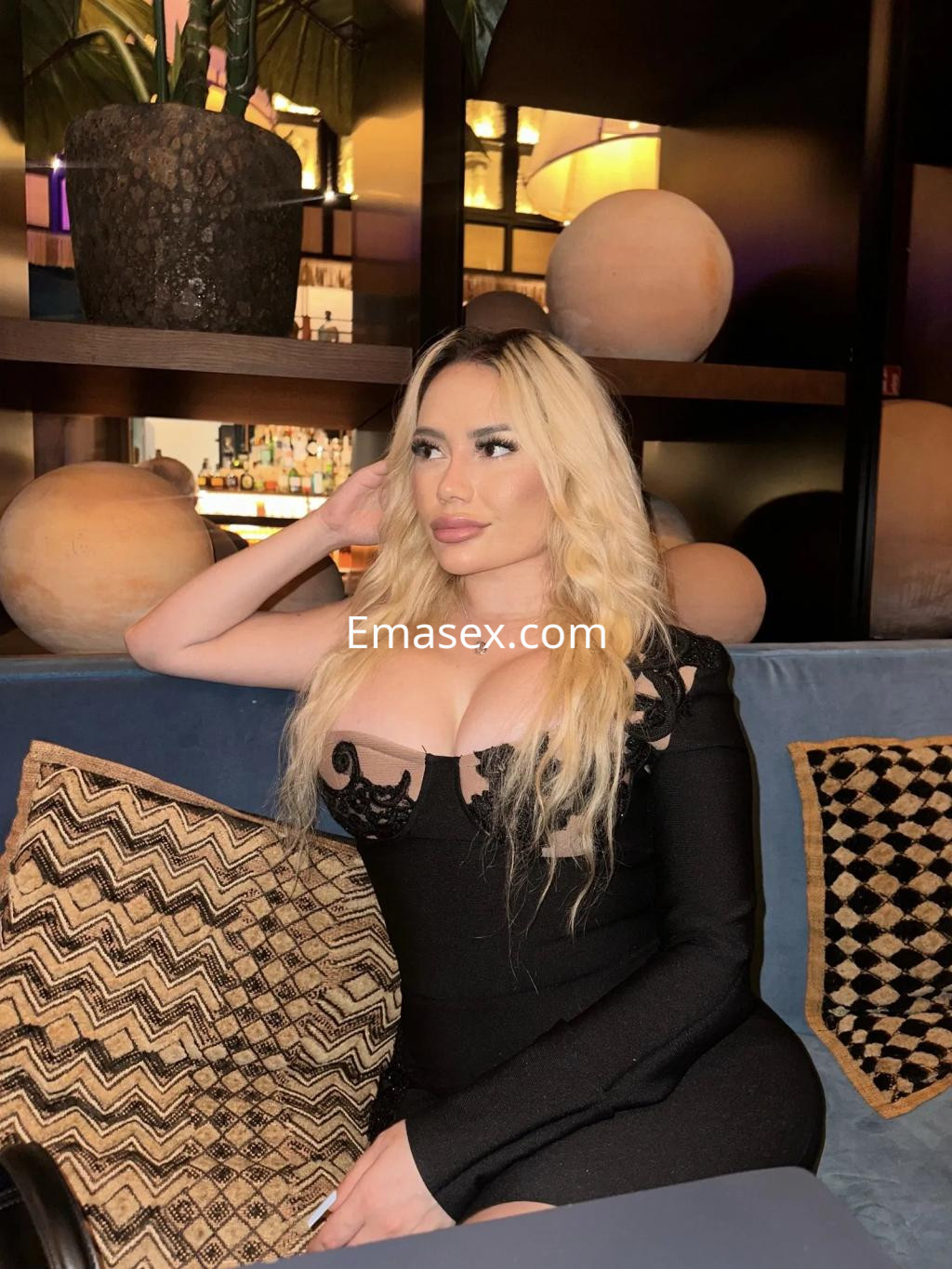 La puta viste un ajustado vestido negro con detalles de encaje, posando en un elegante bar de Valencia.