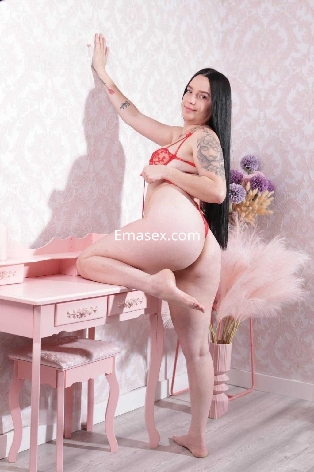 Puta en Zaragoza posa con lencería roja junto a un tocador rosa, mostrando una actitud seductora.