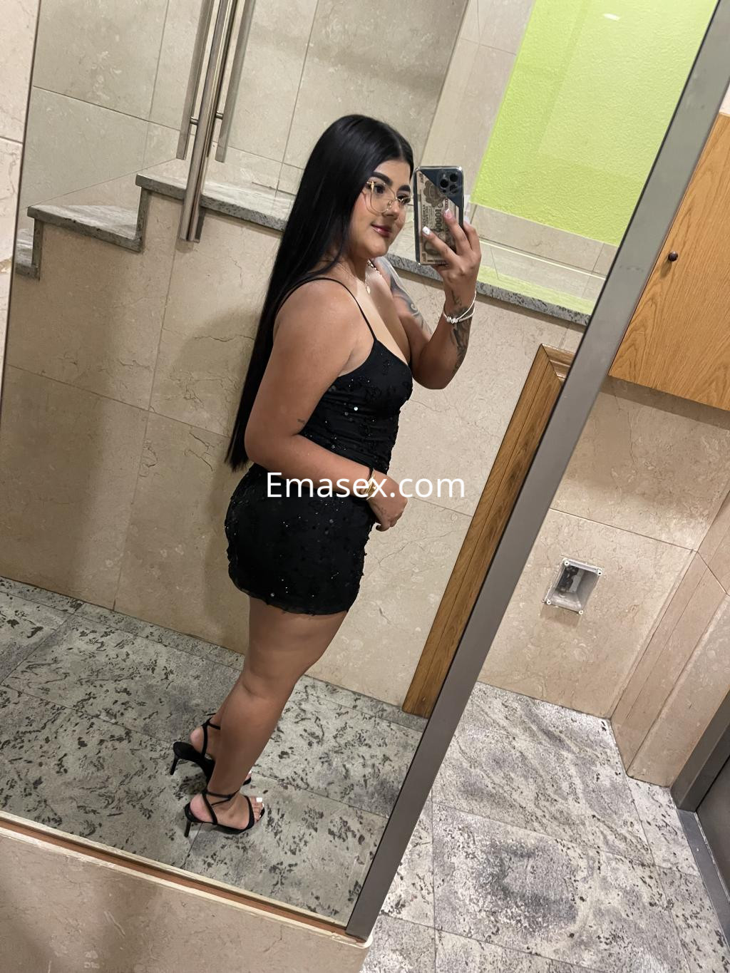 Puta de Irún en un vestido negro ajustado, con cabello largo y lacio, posando frente al espejo.