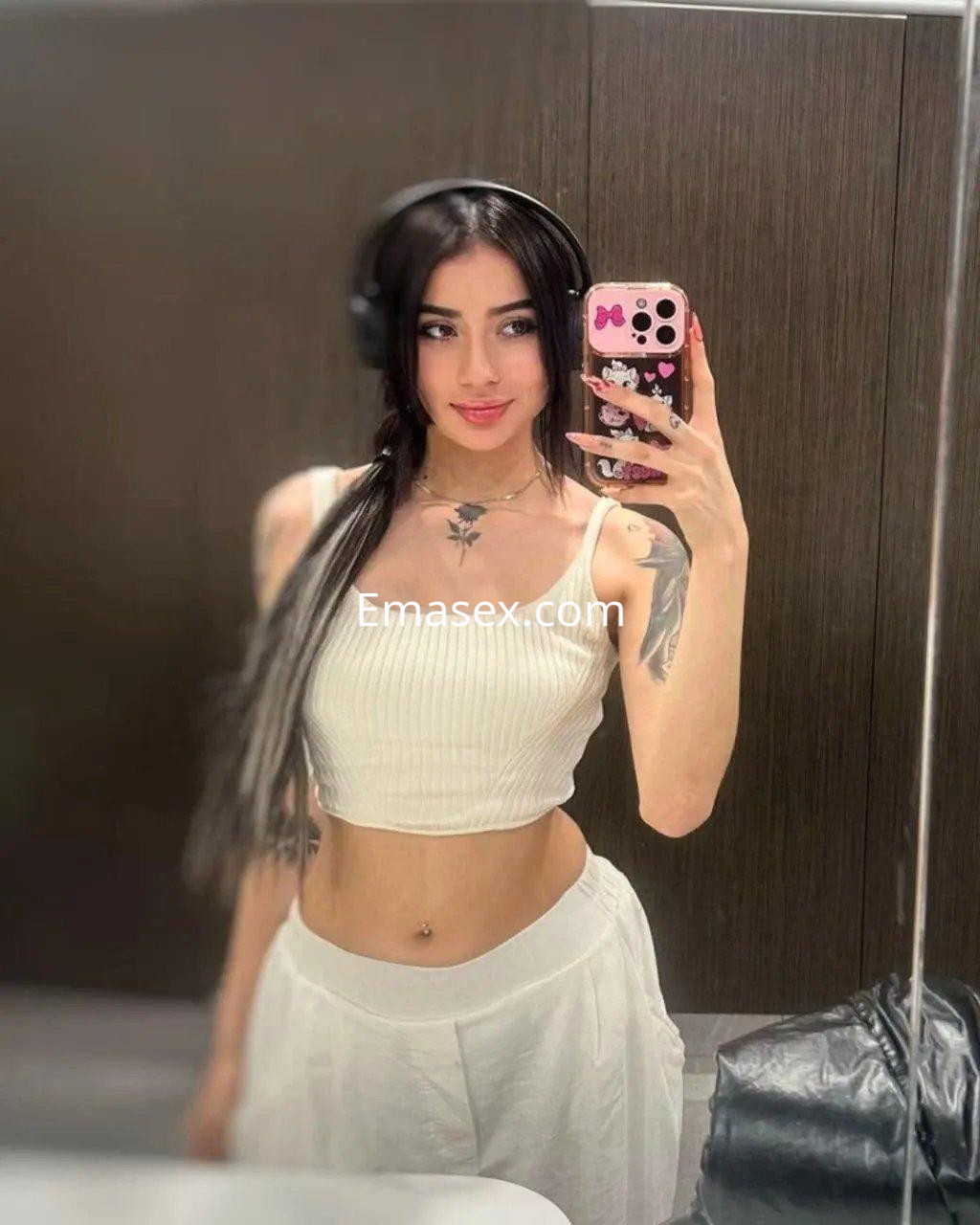Escort en Palma de Mallorca con cabello oscuro, usando un top blanco y falda larga, posando en un espejo.