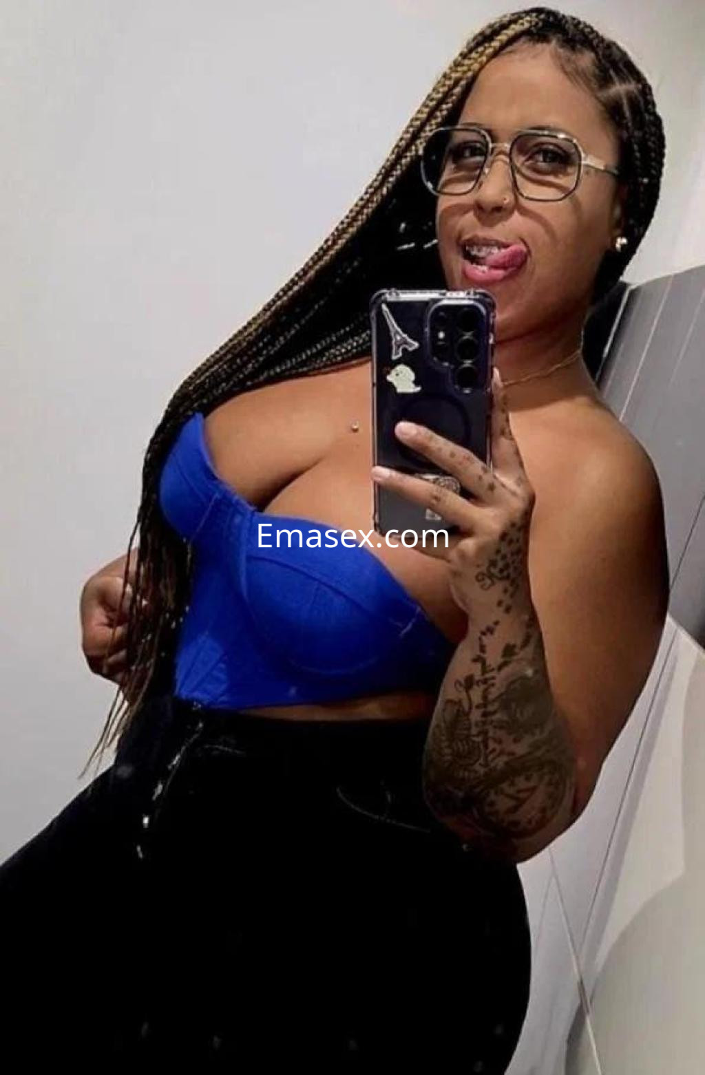Puta con cabello trenzado y gafas, lleva un top azul y jeans oscuros, posando en un espejo en Palma de Mallorca.