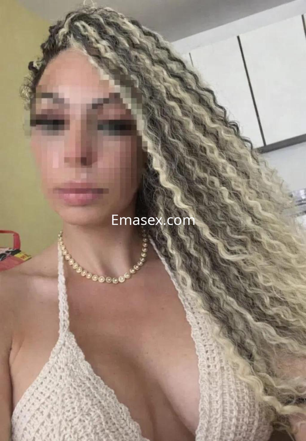Escort en Barcelona con cabello rizado y rubio, luciendo un top de crochet en un entorno interior.
