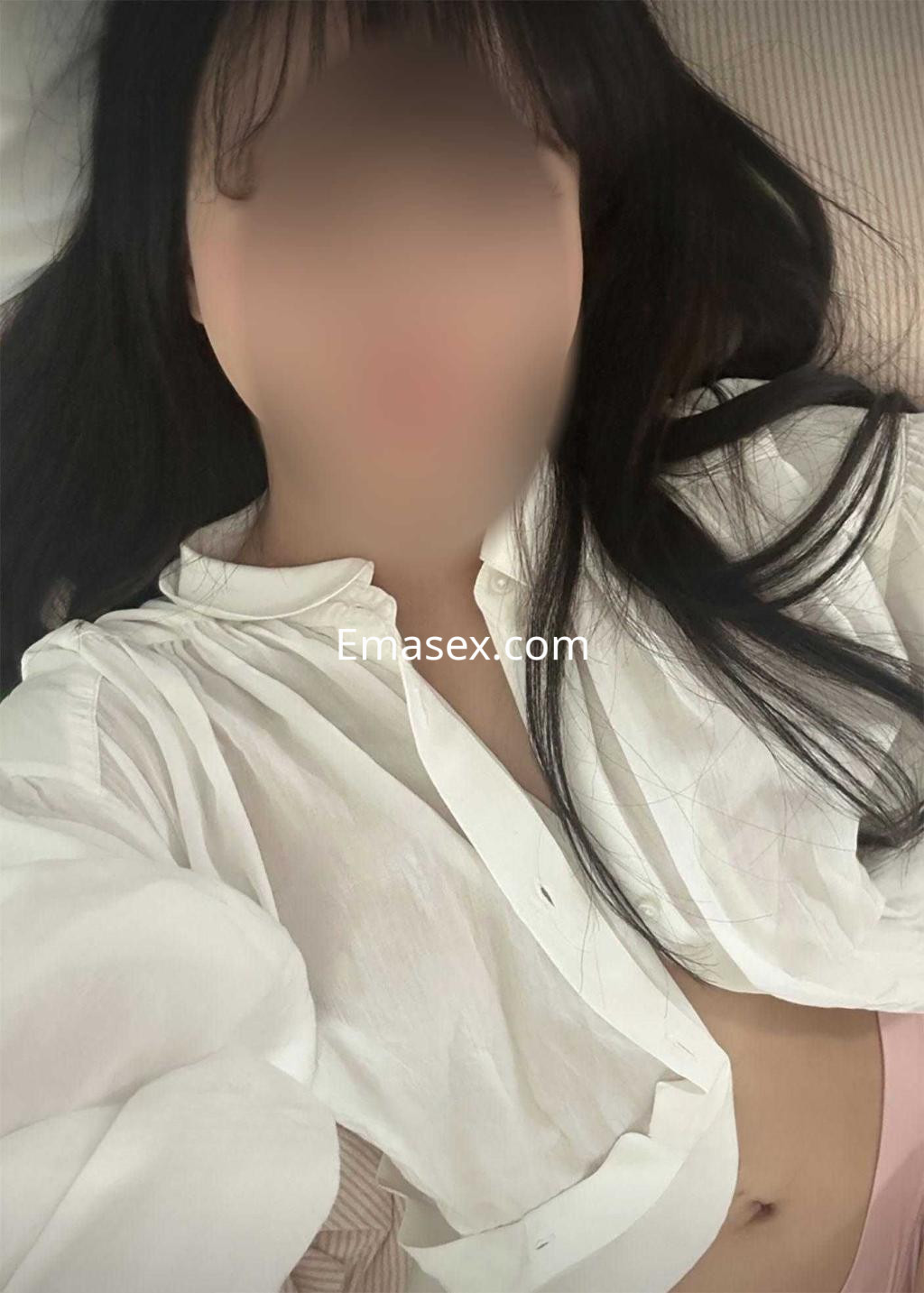 Escort en Barcelona con cabello largo y oscuro, viste una camisa blanca y se encuentra recostada sobre una superficie.