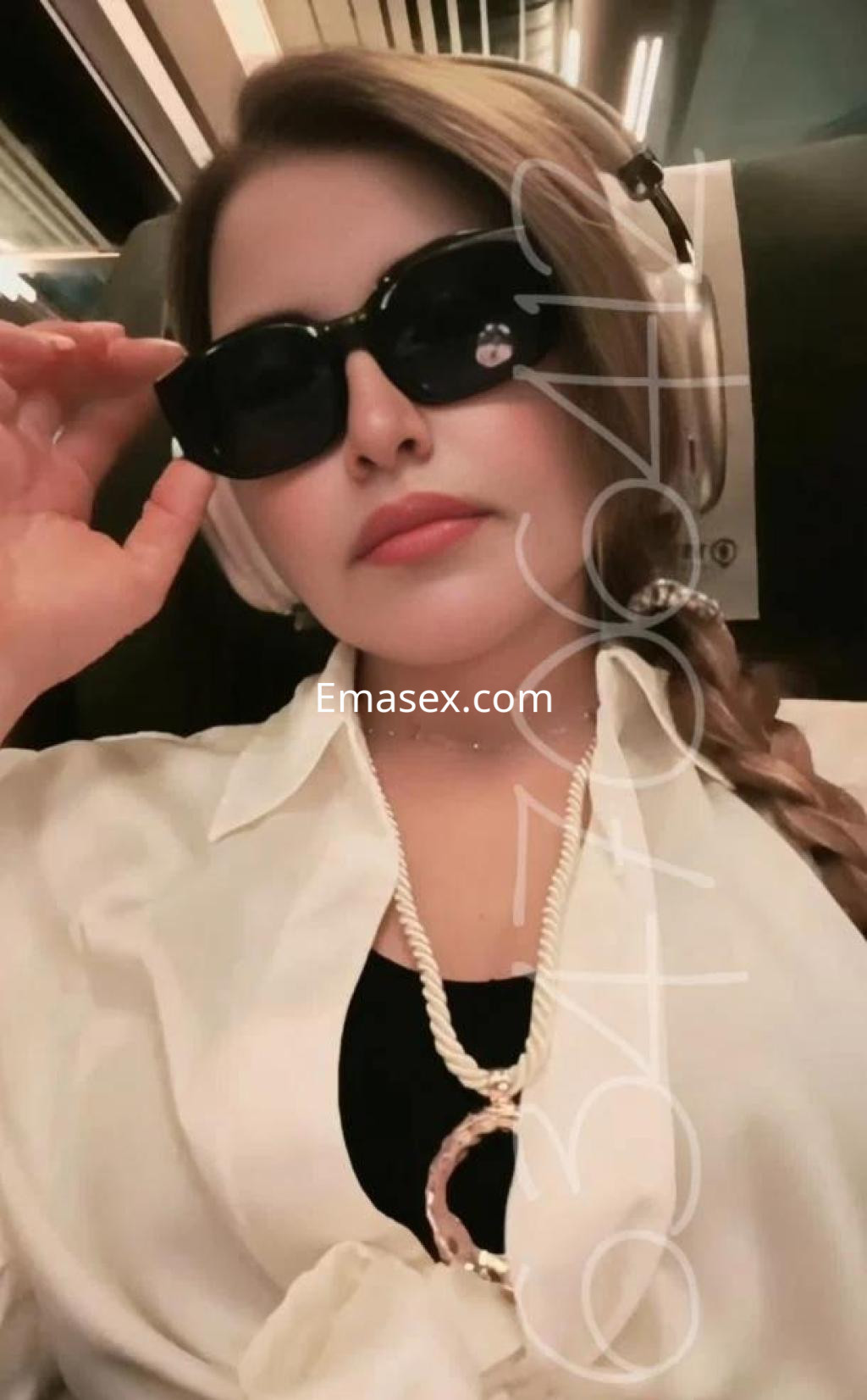La escort luce una blusa blanca y gafas de sol oscuras, mientras viaja en tren en Córdoba.