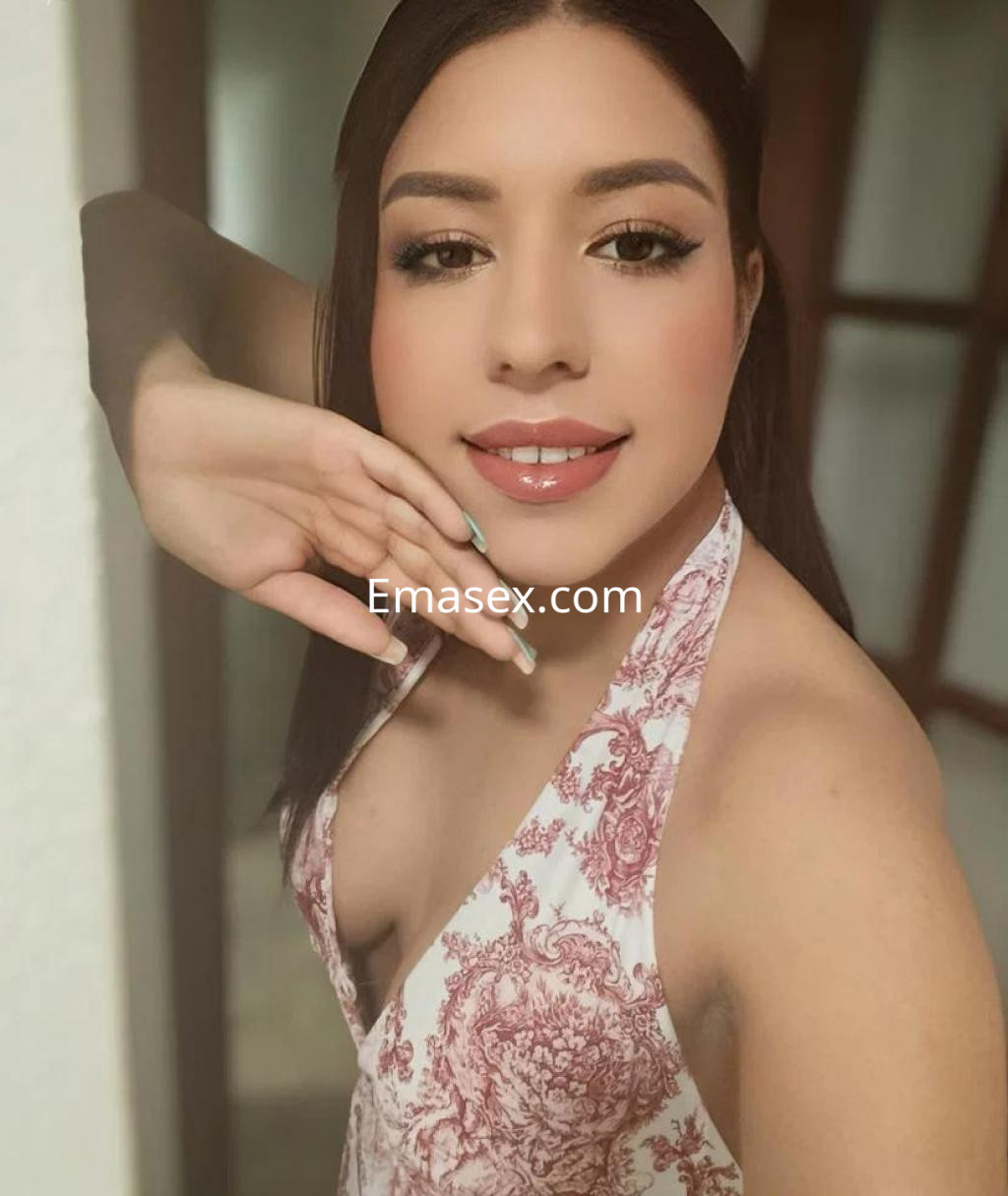 Escort en Huelva posando con una blusa de tirantes estampada, mostrando una sonrisa y su cabello lacio.