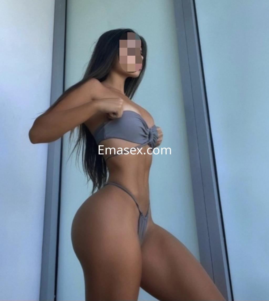 Escort en Lleida posa de perfil en bikini gris, mostrando una figura esculpida y cabello largo.