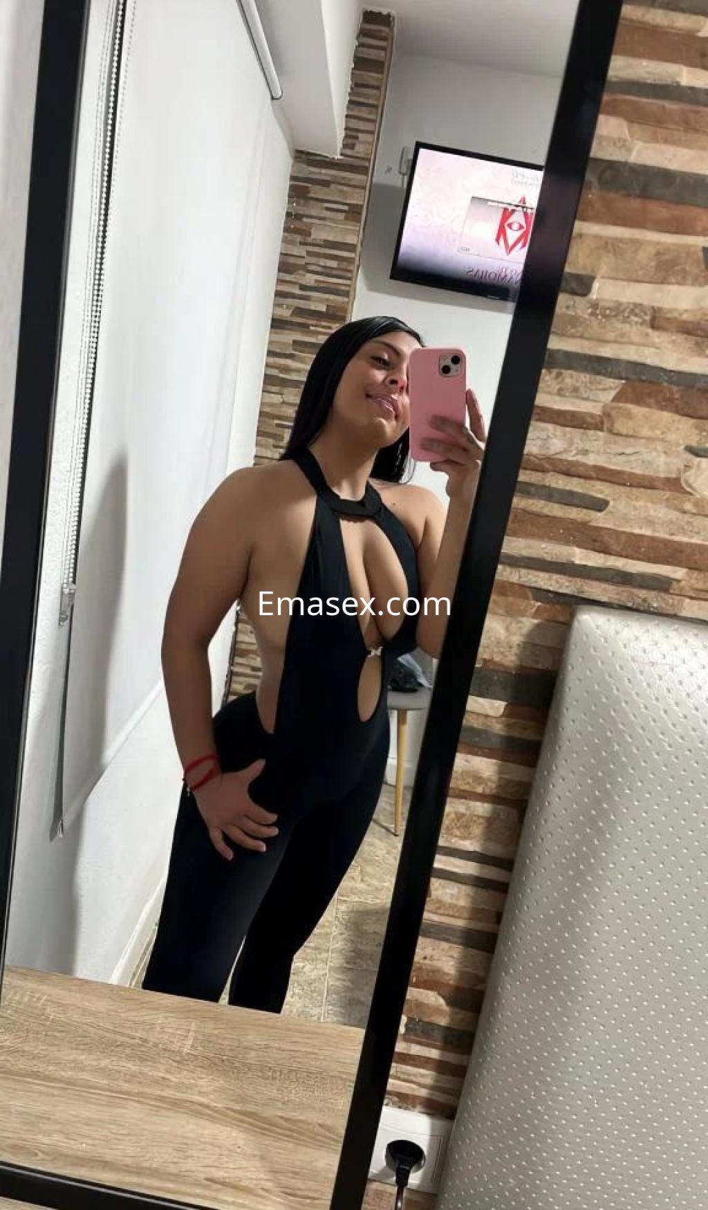 Escort en Málaga posando frente a un espejo, vistiendo un mono negro con cortes laterales y cabello oscuro.