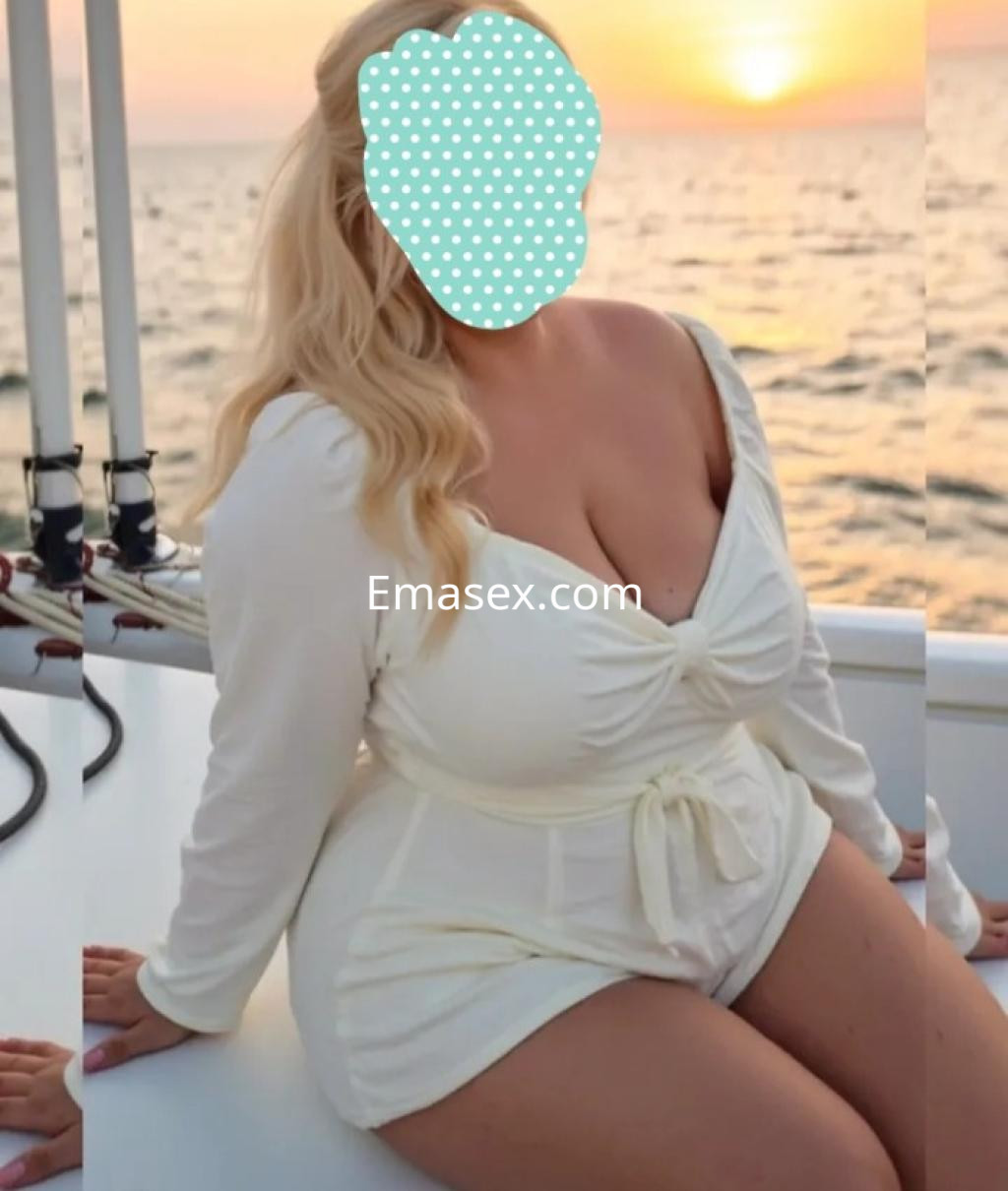 Escort en Bilbao con cabello rubio y lacio, vestida con un conjunto blanco, disfrutando del atardecer en un barco.