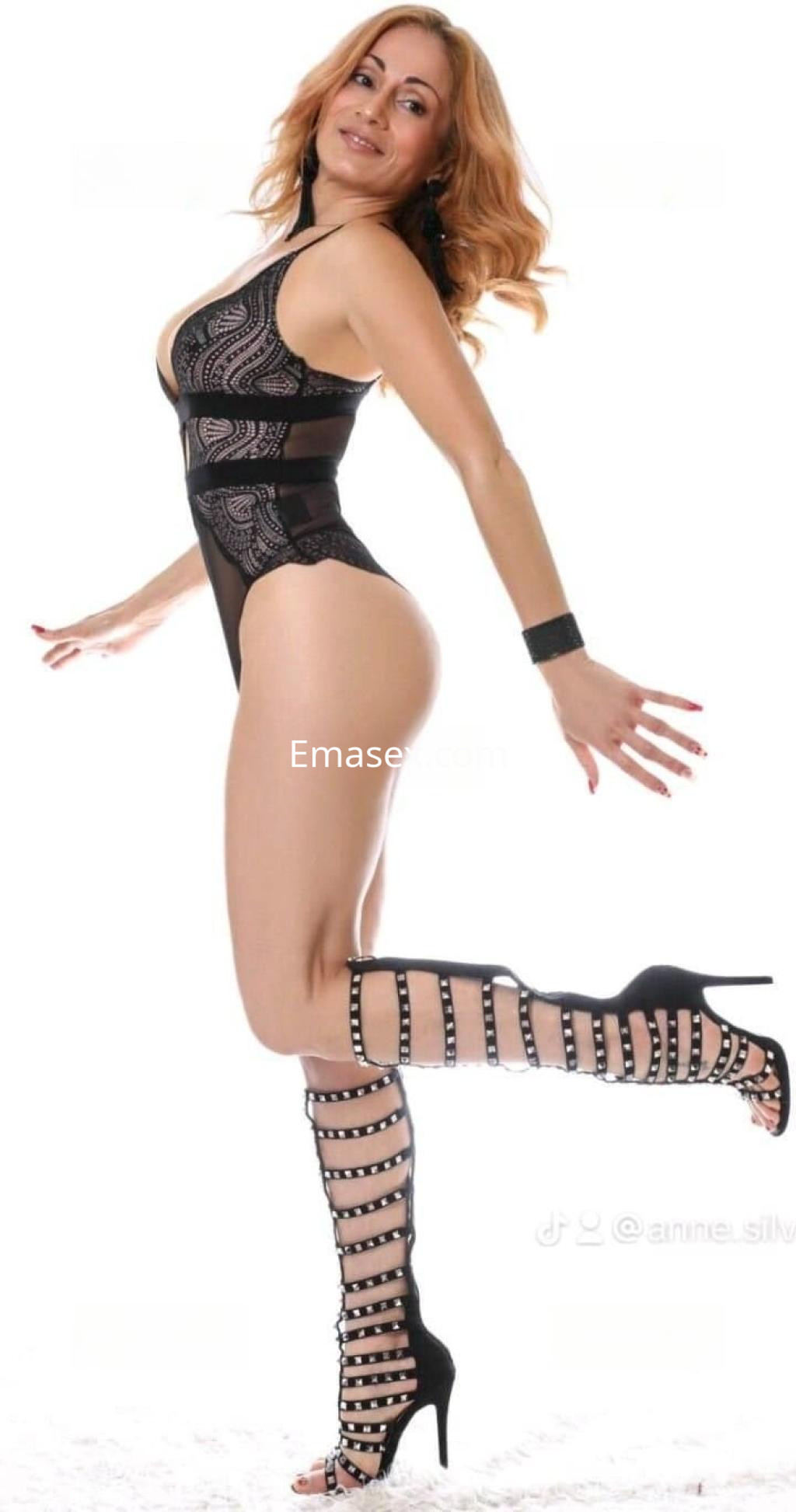 Escort en Zaragoza posando con un body negro decorado, medias altas y tacones, mostrando una actitud divertida.