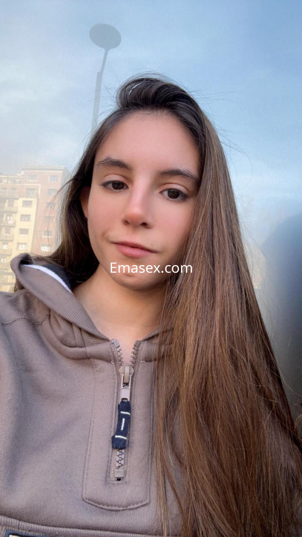 Escort en Bilbao con cabello largo y lacio, vestida con sudadera gris, posando frente a un fondo urbano.
