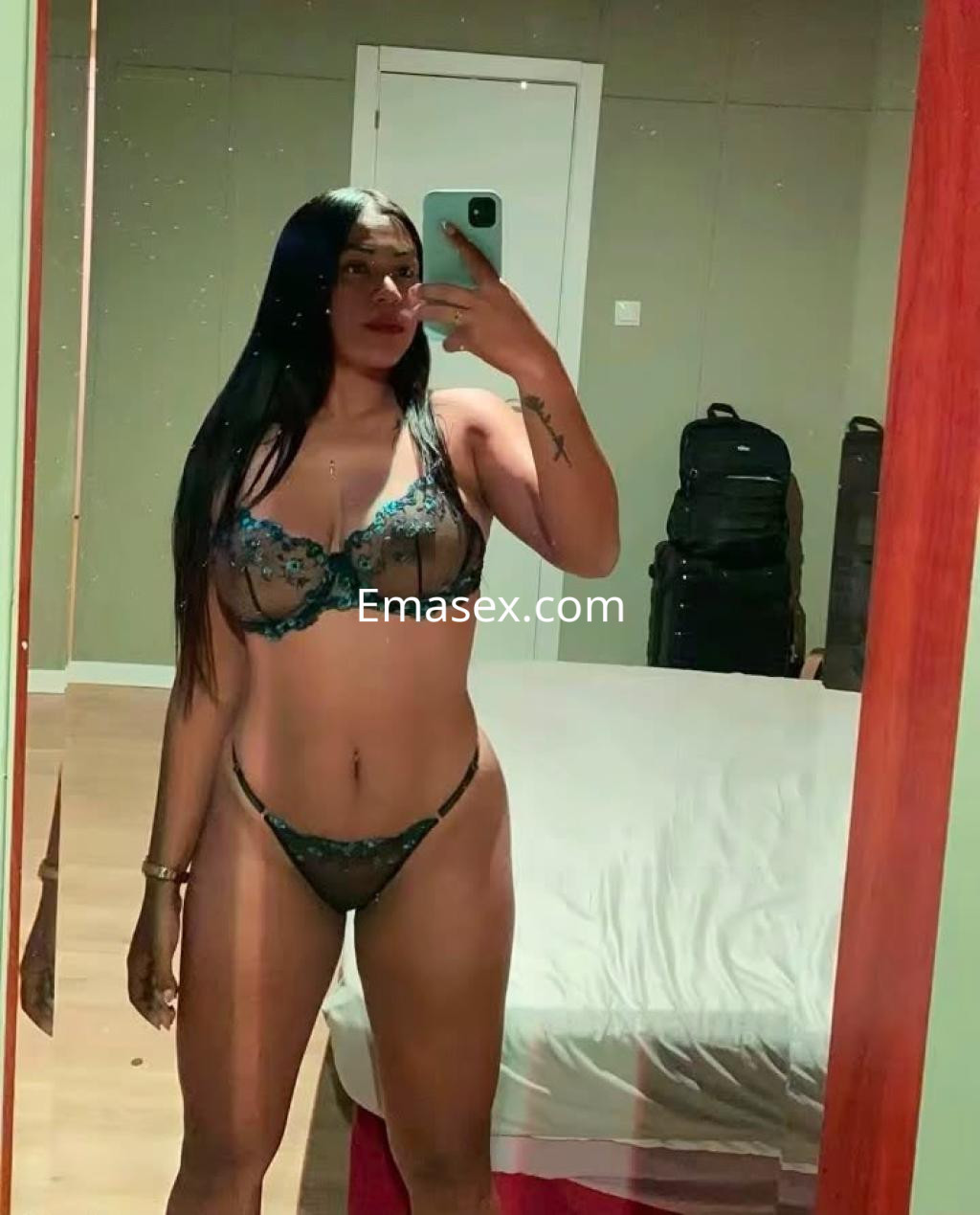 La escort en Irún luce un conjunto de lencería negra con detalles en azul, posando frente al espejo.