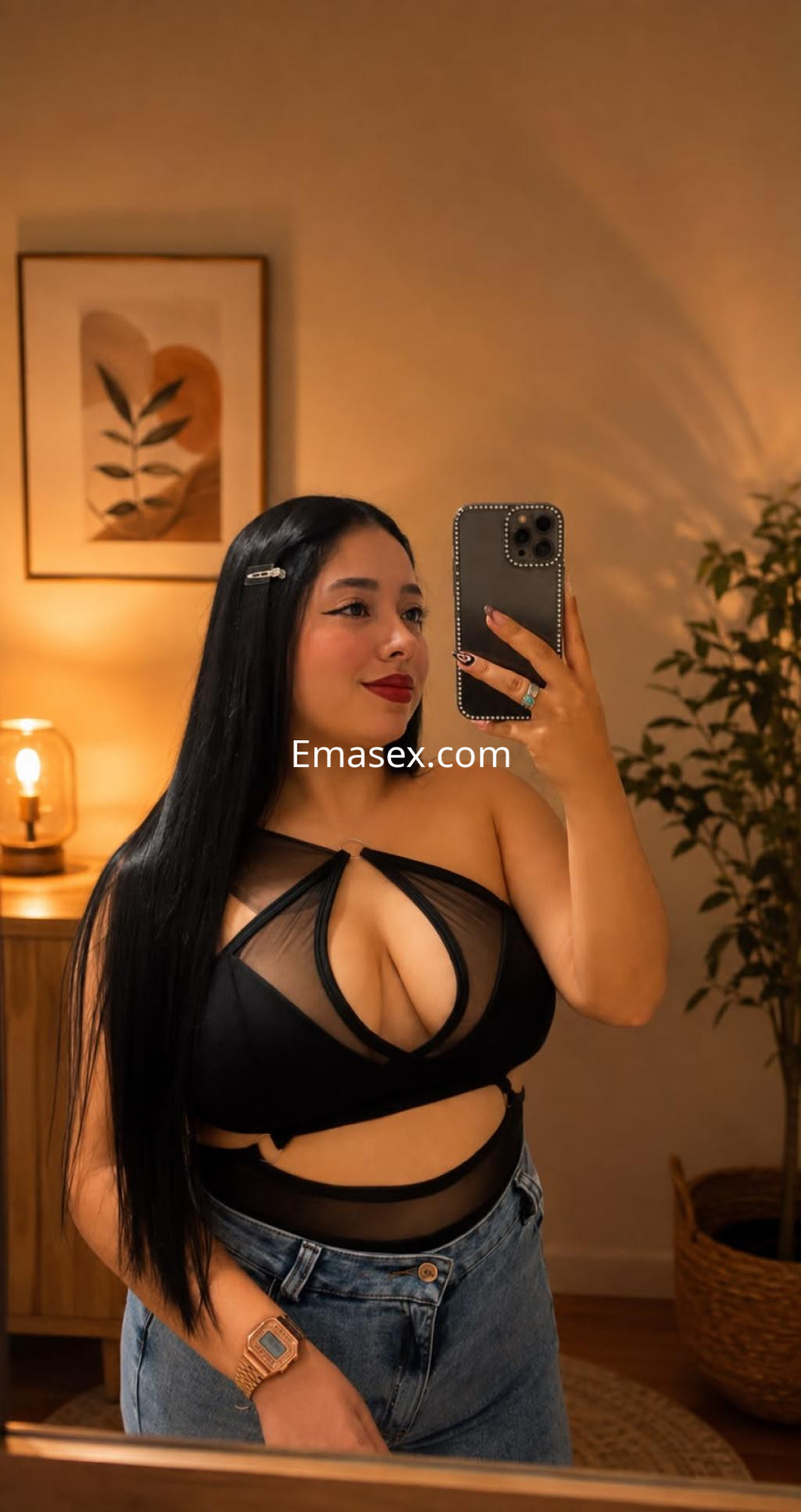 Escort en Bilbao con cabello largo y lacio, vistiendo un top negro transparente y jeans de tiro alto, posando frente a un espejo.