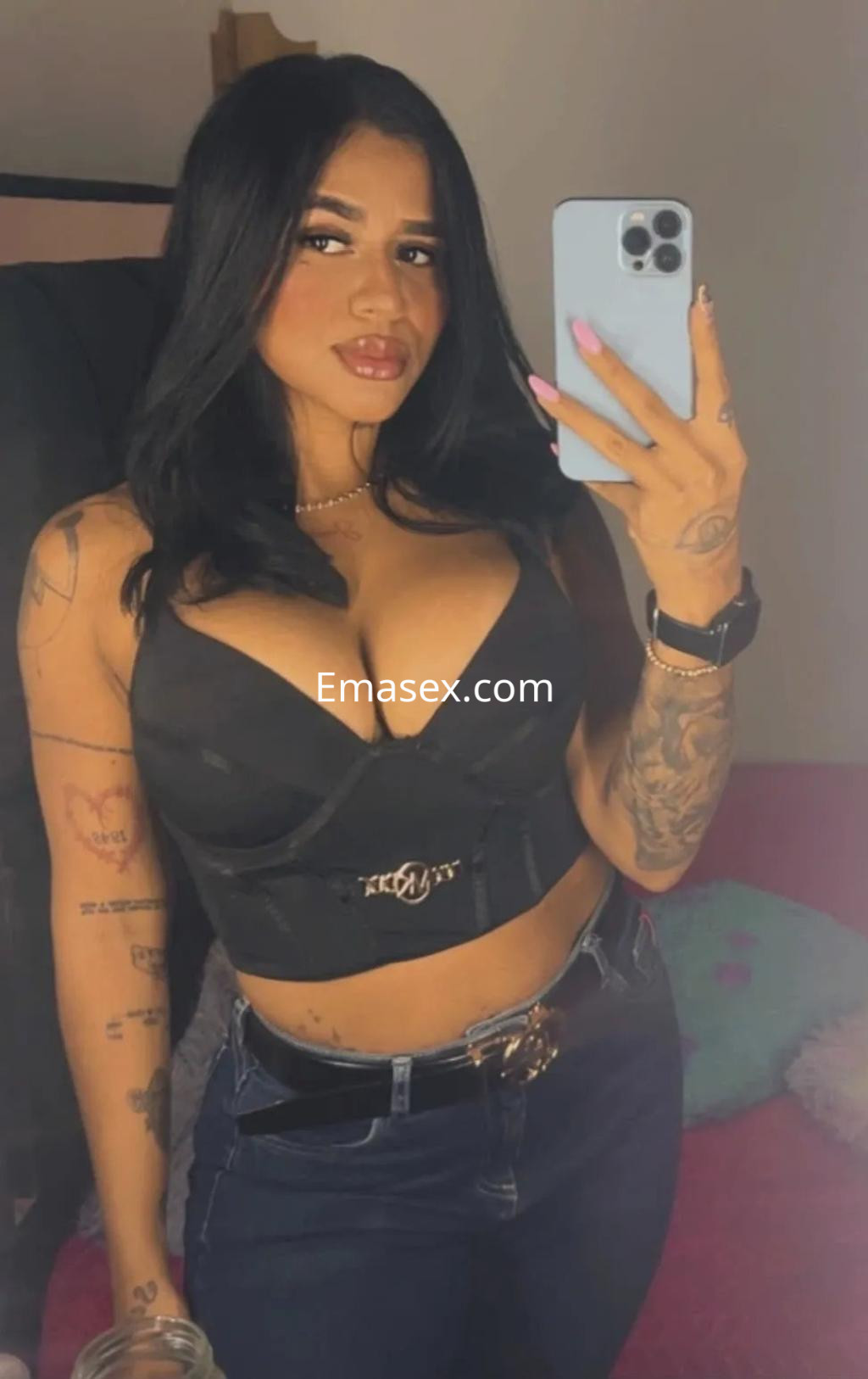 Escort en Gijón con cabello oscuro, top negro ajustado y pantalones vaqueros, posando frente a un espejo.