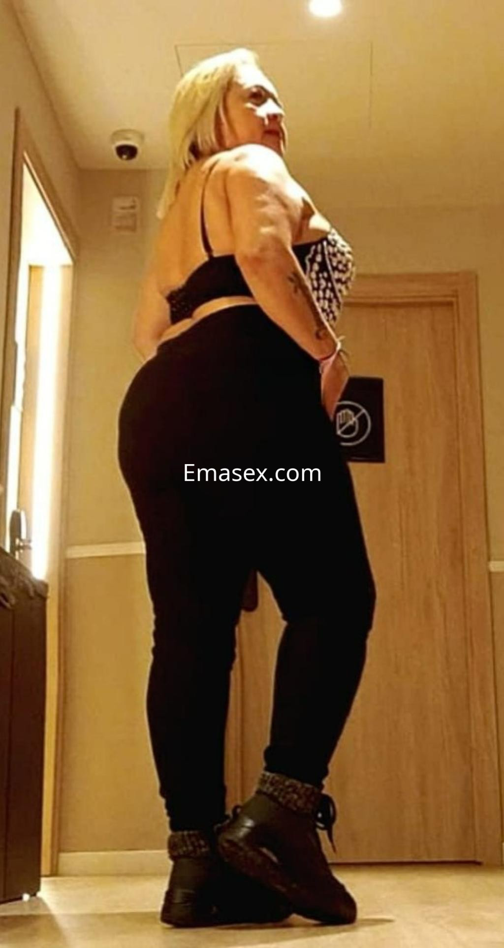 Escort en Zaragoza con cabello rubio, viste una blusa de tirantes y leggings negros, posando de perfil.