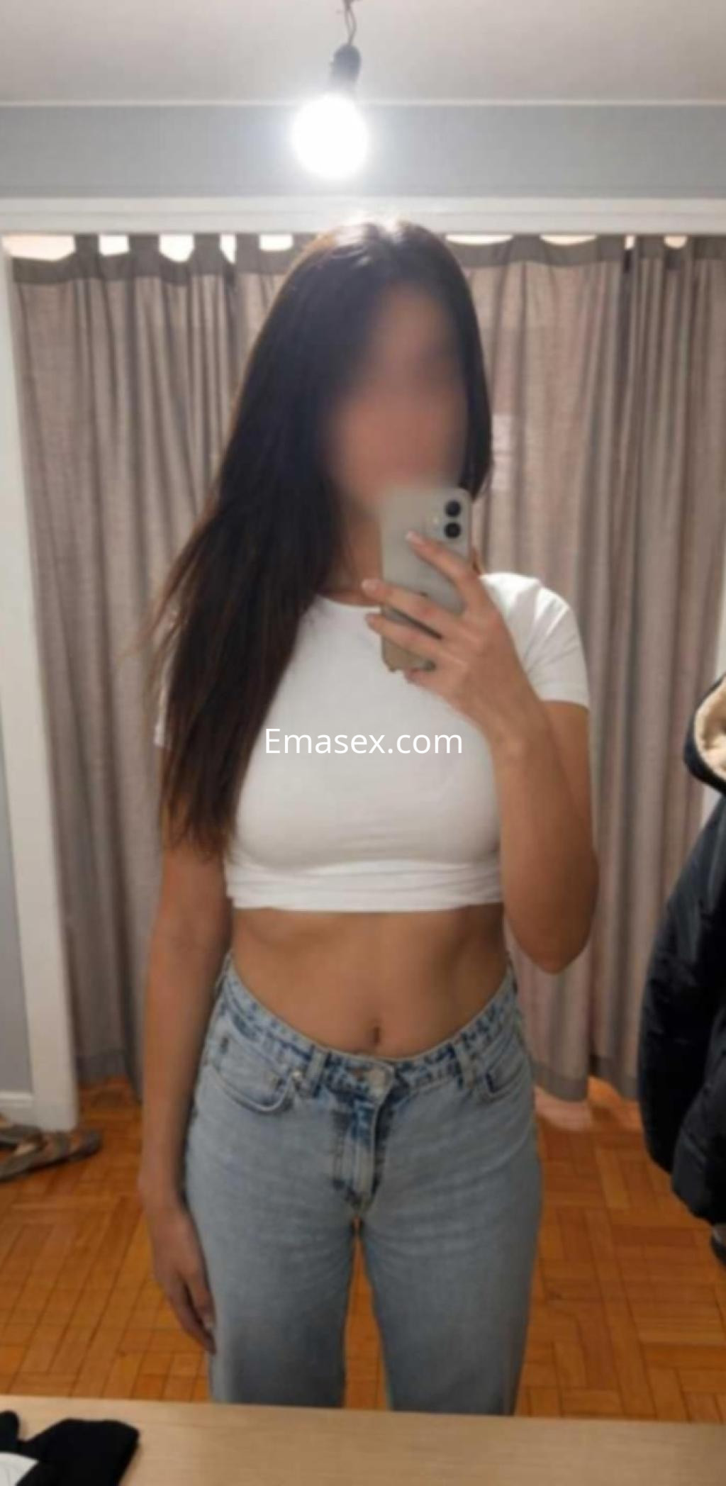 Escort en Vigo con cabello largo y lacio, viste una camiseta blanca ajustada y jeans claros, posando frente al espejo.