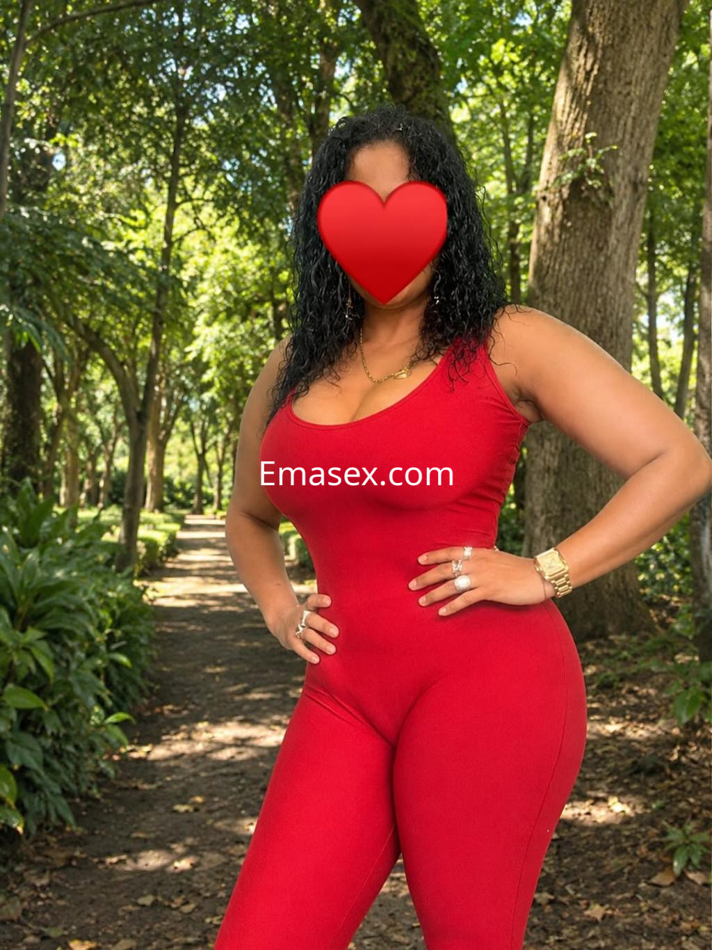 Escort en Bilbao con cabello rizado y oscuro, vistiendo un ajustado mono rojo en un entorno natural.