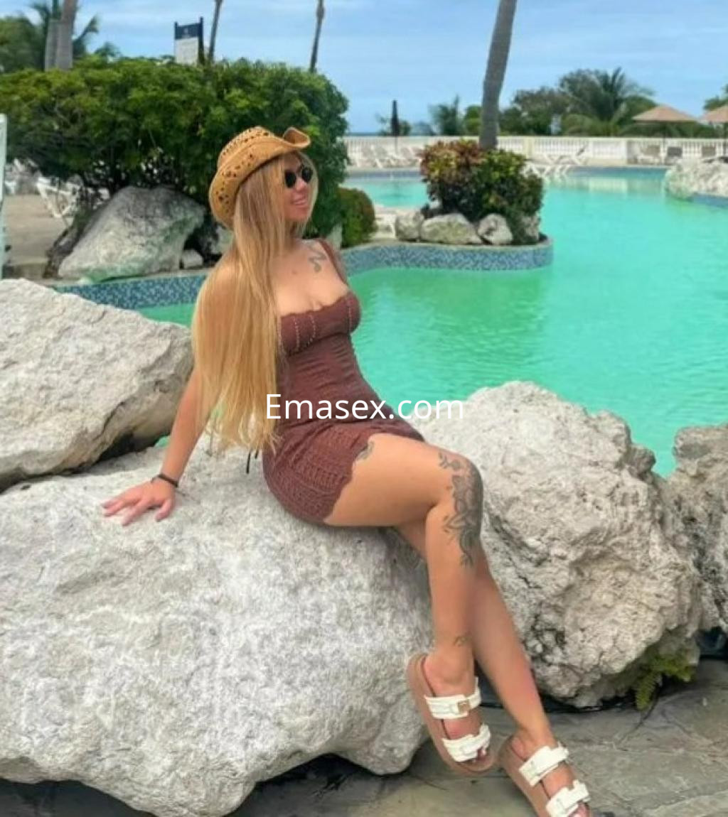 La puta posa sentada sobre una roca junto a una piscina en Zaragoza, luciendo un vestido marrón y sandalias.