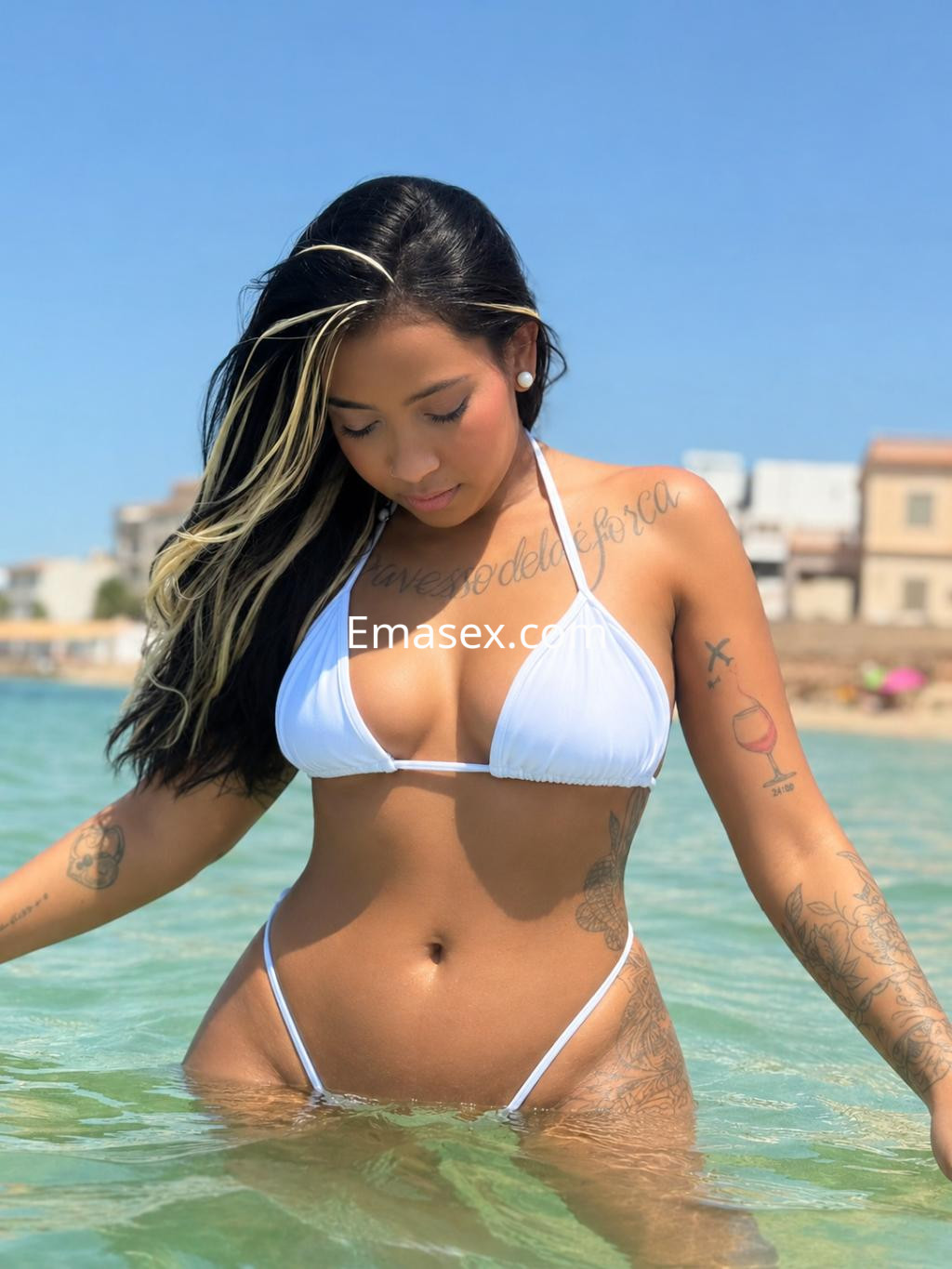 La puta en Palma de Mallorca luce un bikini blanco mientras se encuentra en el agua, mostrando sus tatuajes.