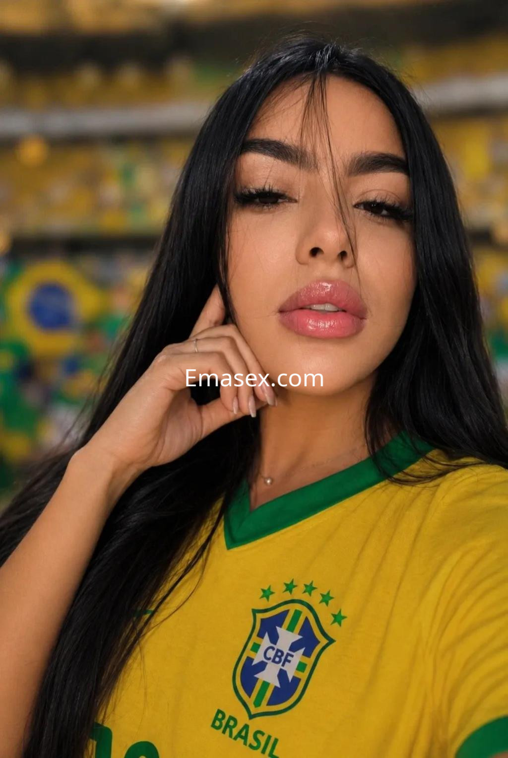 Escort en Alicante con una camiseta amarilla de Brasil, posando con el cabello largo suelto y un fondo deportivo.