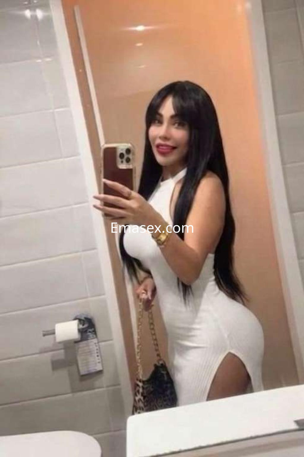 Escort en Ibiza posando en un espejo, vistiendo un vestido blanco ajustado con un corte lateral y cabello largo.