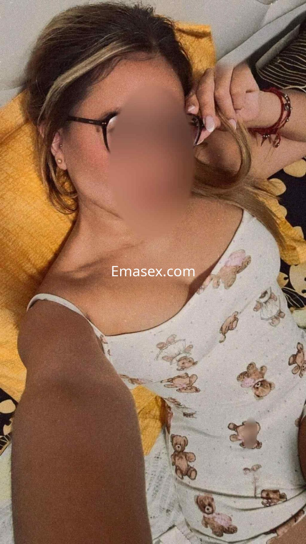Escort en Barcelona, posando en la cama con un vestido de tirantes con estampado de ositos y gafas.