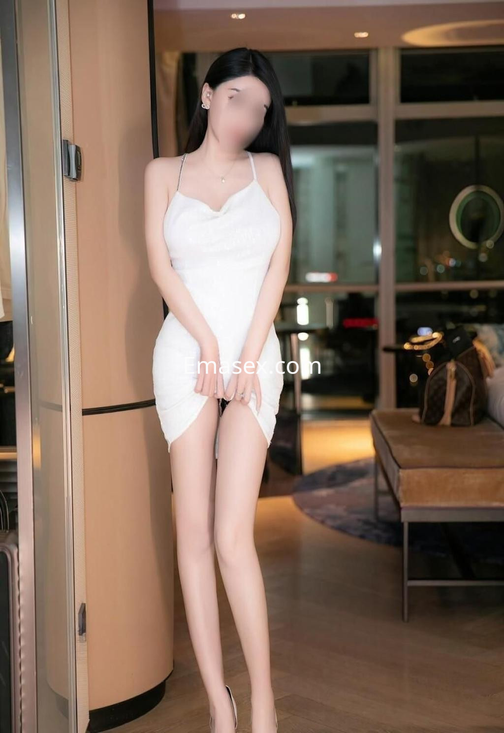 Escort en Barcelona luciendo un vestido blanco ajustado, con tirantes finos y un fondo elegante.
