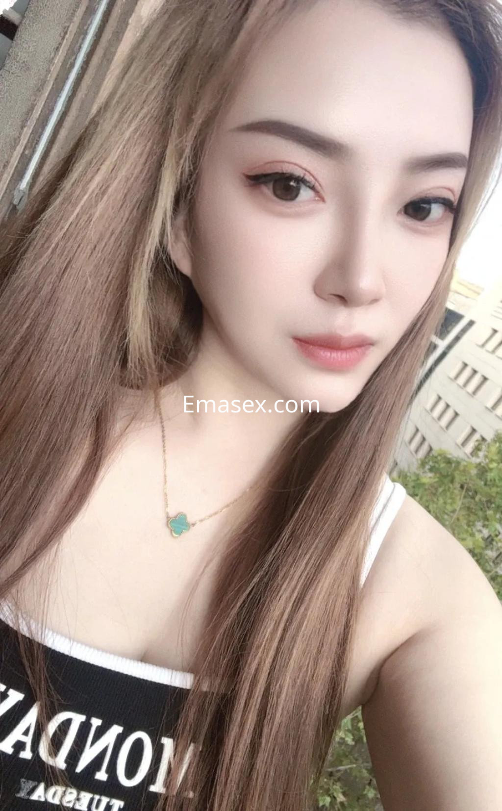 Escort en Barcelona con cabello largo y lacio, luciendo un top negro y un collar delicado, sonríe a la cámara.