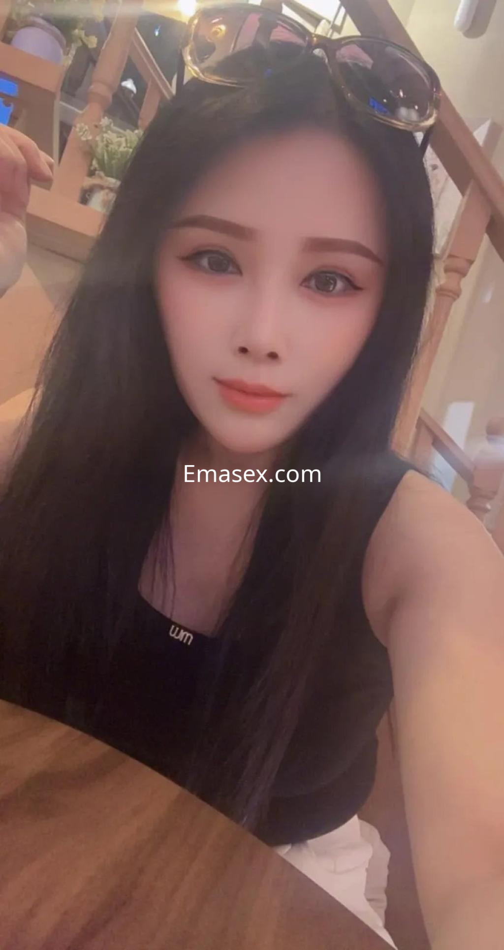 Escort de Barcelona con cabello largo y lacio, usando un top negro, tomando una selfie en un entorno interior.