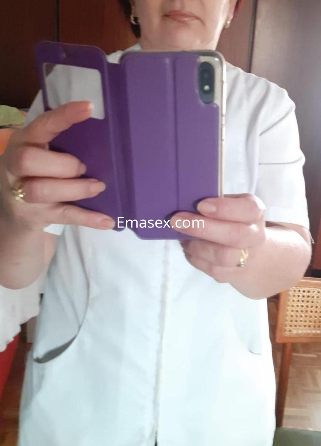 La puta en Burgos se toma un autorretrato con un teléfono, vistiendo una blusa blanca y mostrando un fondo colorido.