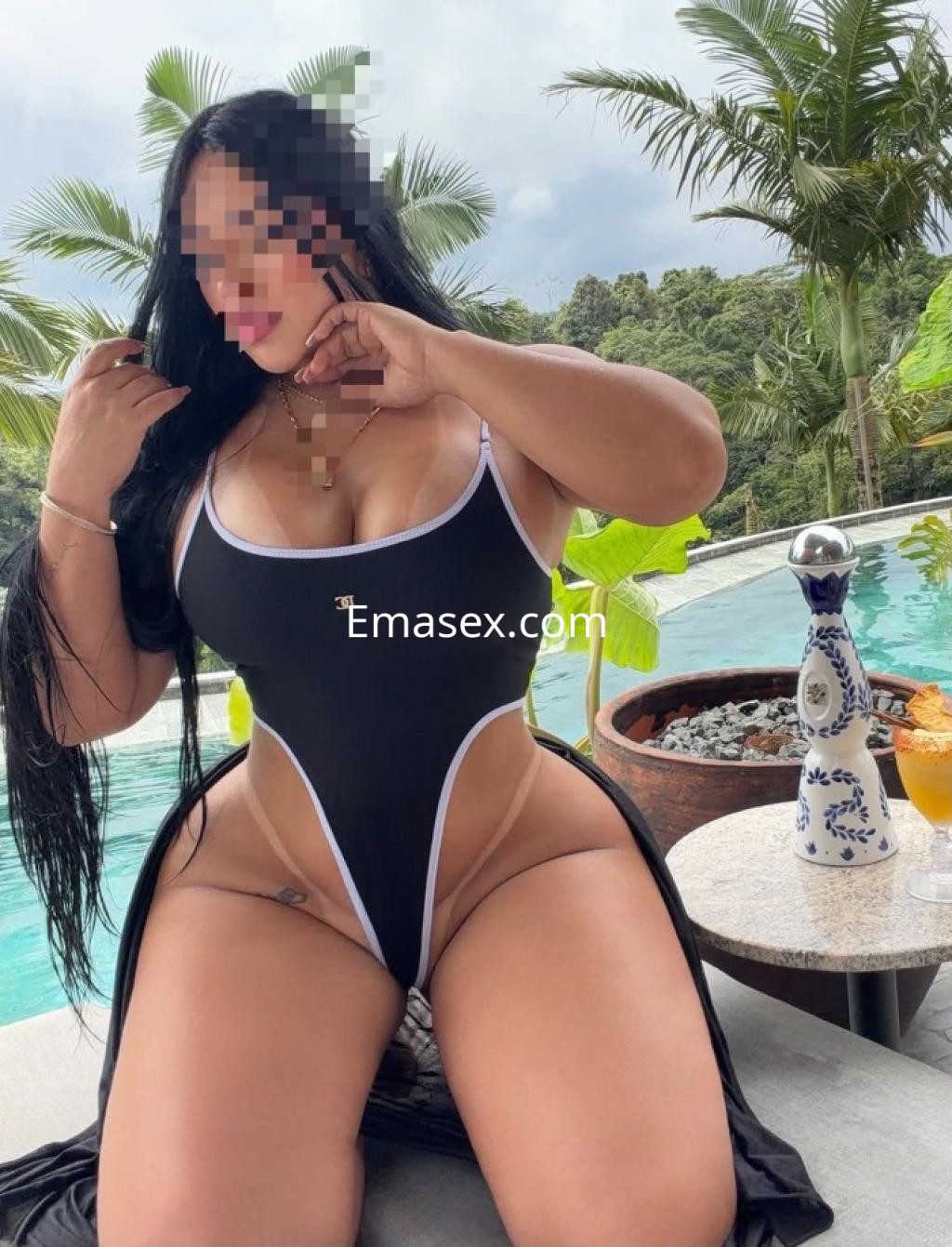 Escort en Huelva posando junto a una piscina, luciendo un traje de baño negro con detalles blancos.