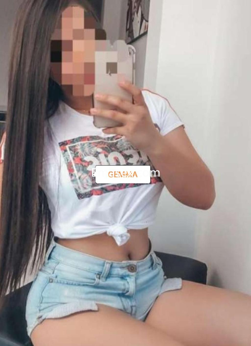 Puta con cabello largo y lacio, viste camiseta blanca y shorts de mezclilla, sentada en Lleida.