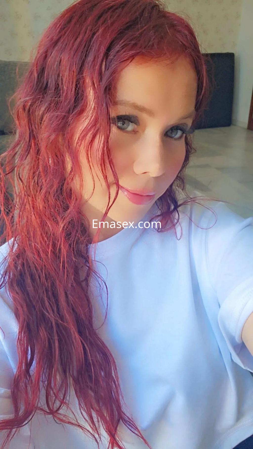 La puta se toma un selfie con el cabello rizado y rojo, vistiendo una camiseta blanca en Málaga.