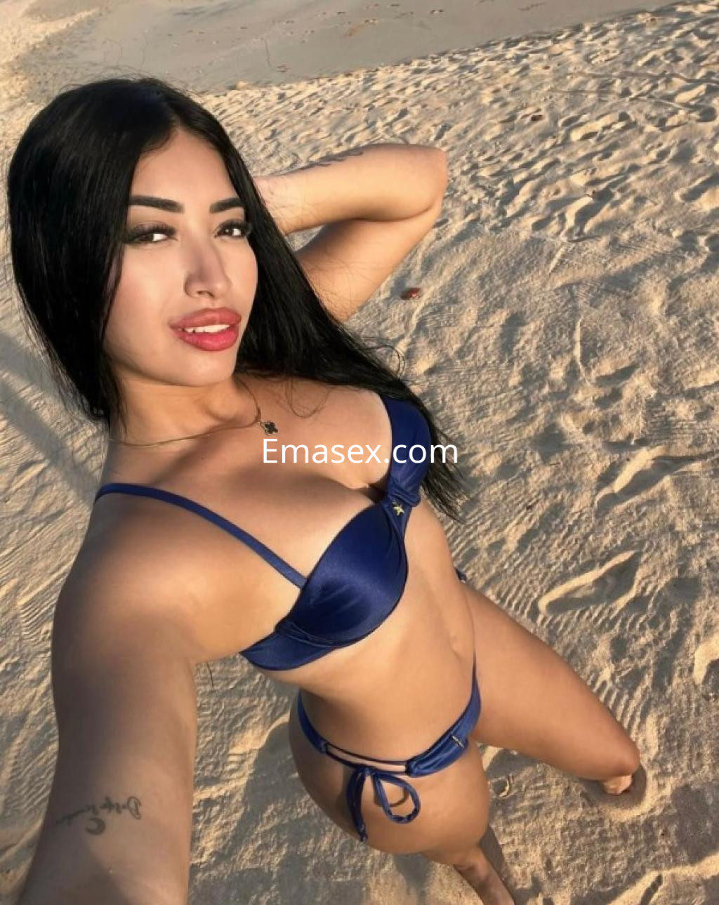 La puta posa sonriente en la playa, luciendo un bikini azul y con el cabello largo y negro.