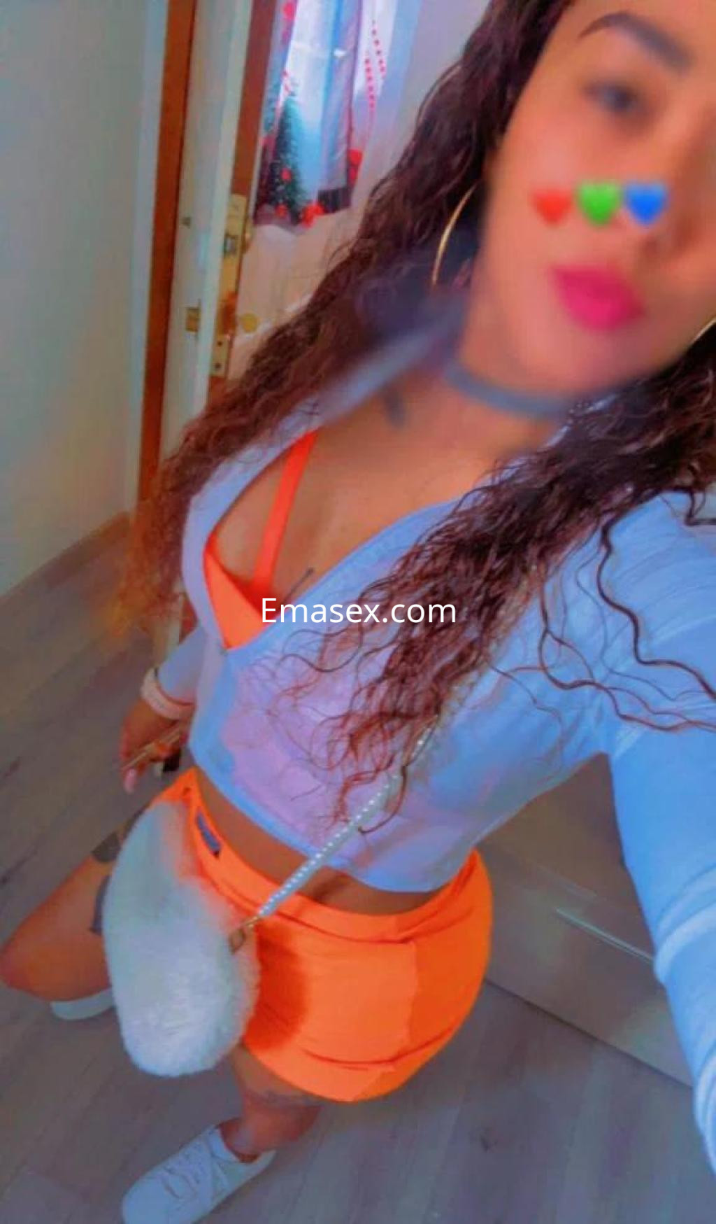 Escort en Pontevedra vistiendo un top azul y una falda corta naranja, con cabello rizado y accesorios brillantes.
