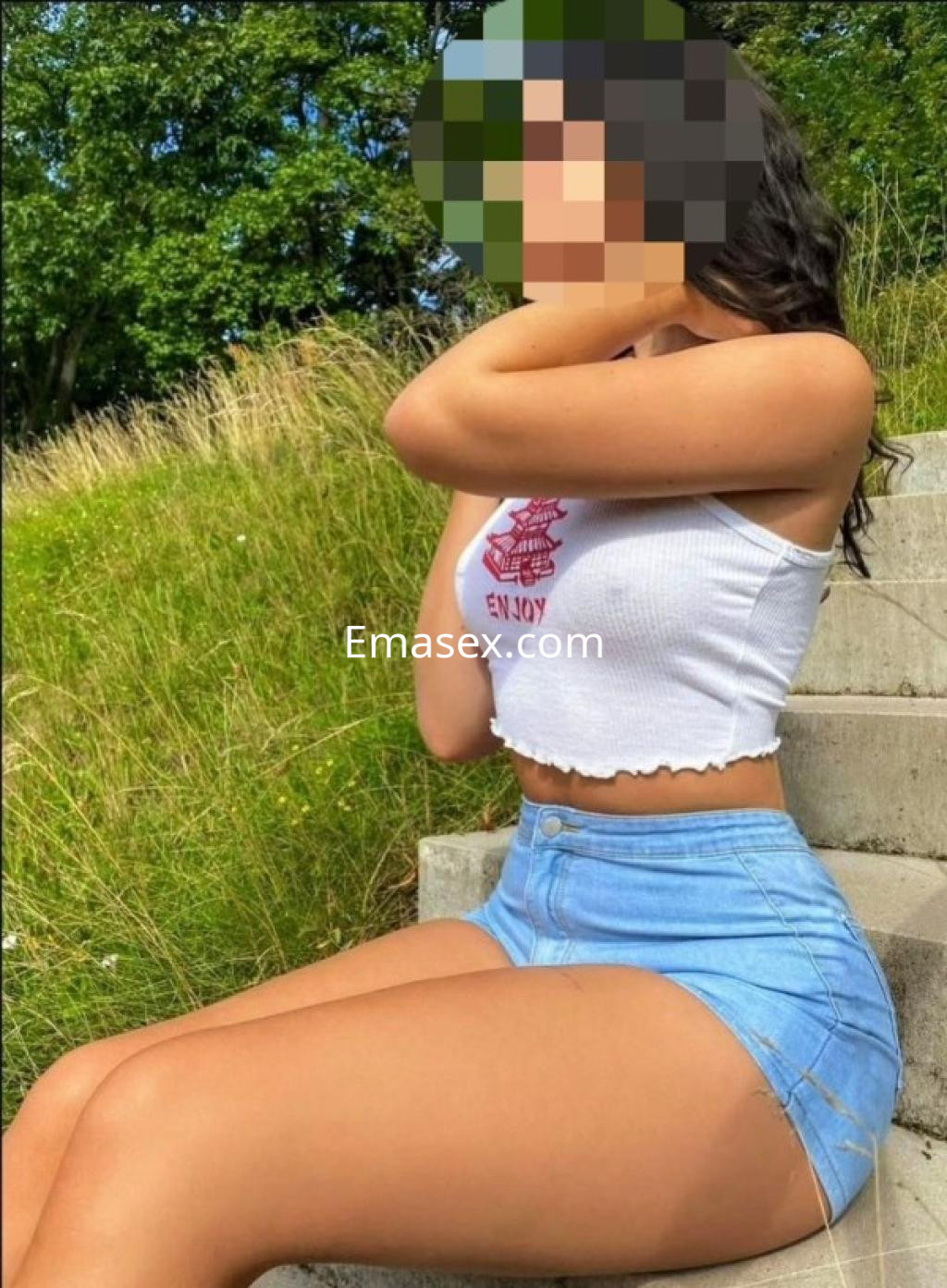 Escort en Tarragona sentada en escaleras, vistiendo un top blanco y una falda corta de mezclilla, rodeada de naturaleza.
