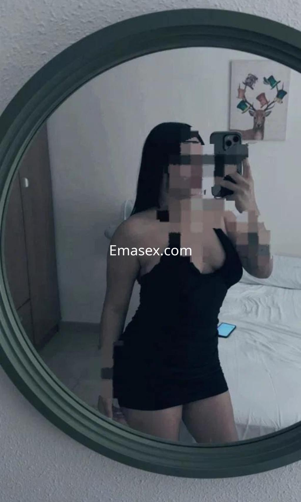 Puta en Tarragona se mira al espejo con un vestido negro ajustado, mostrando su figura y cabello largo.