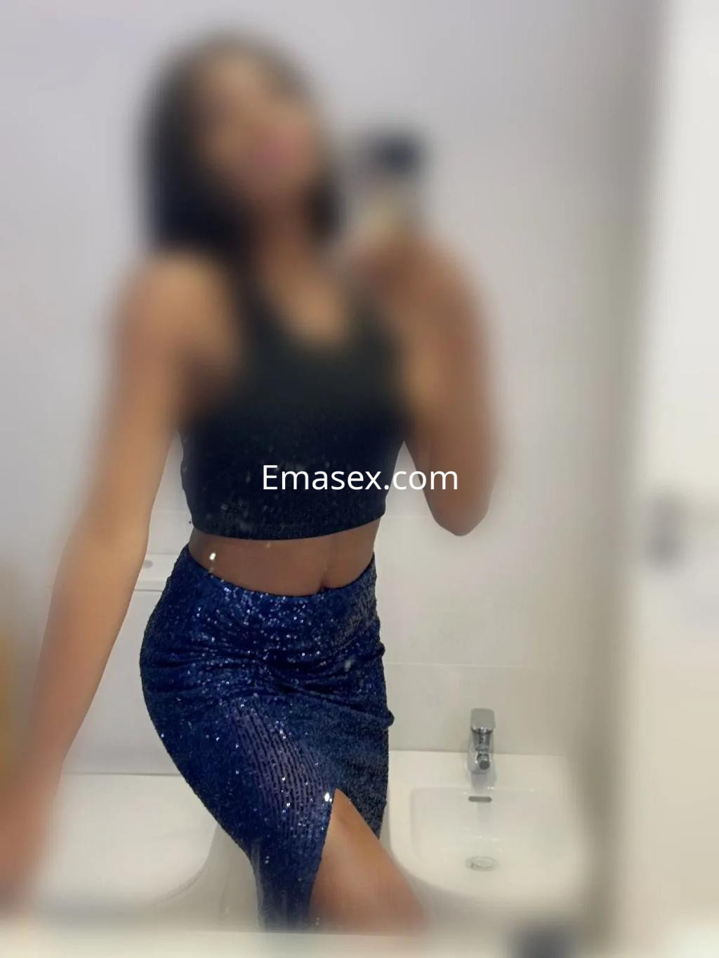 Escort en Valencia, posando con una blusa negra y una falda brillante, mostrando un estilo elegante y moderno.
