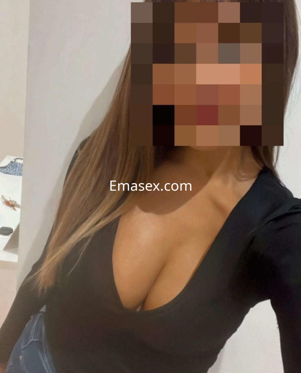Puta en Valencia con cabello largo y lacio, vistiendo un top negro de escote profundo y fondo neutro.
