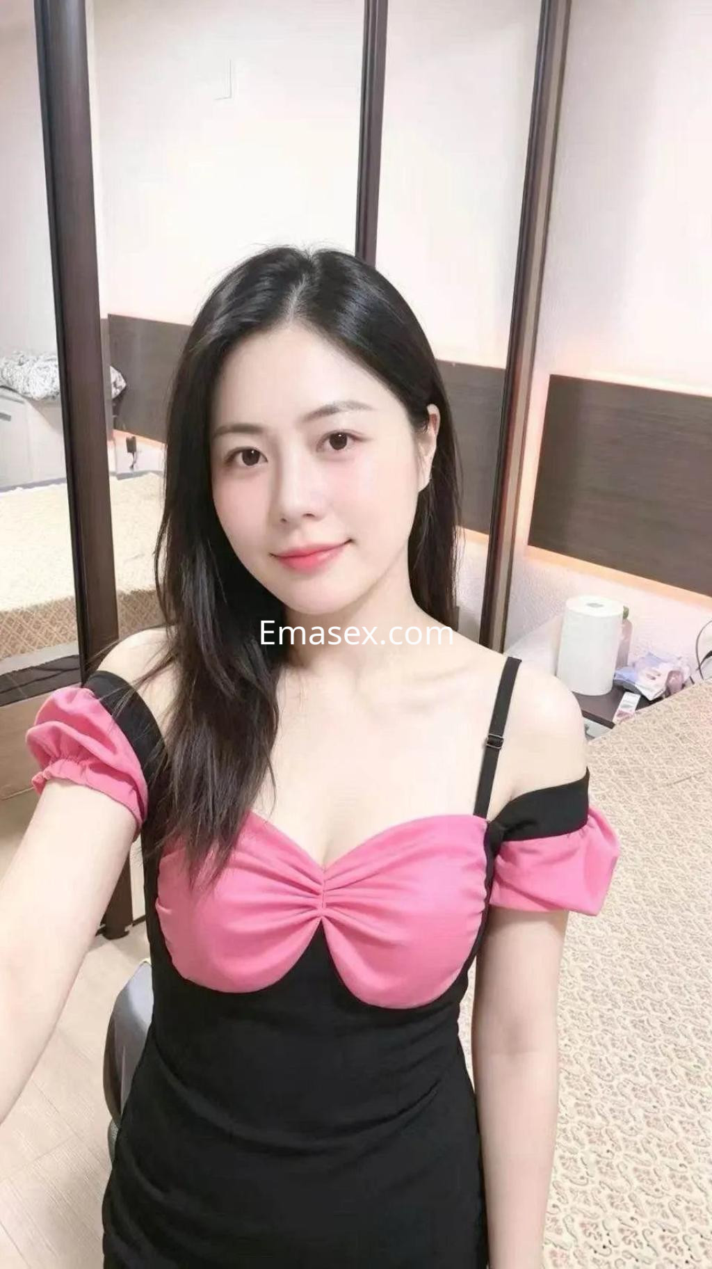 Escort en Valencia con cabello negro y lacio, viste un vestido ajustado negro y rosa, en un entorno interior.