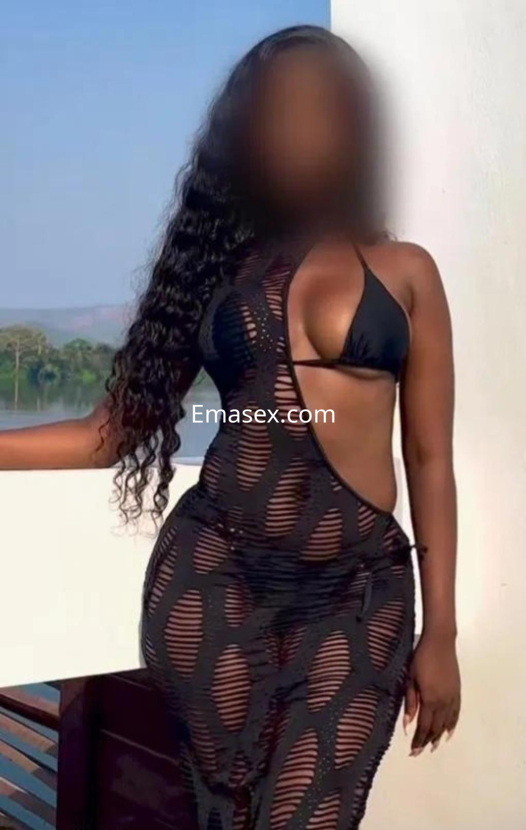 Puta en Girona con cabello rizado y largo, vistiendo un vestido negro transparente que resalta su figura.