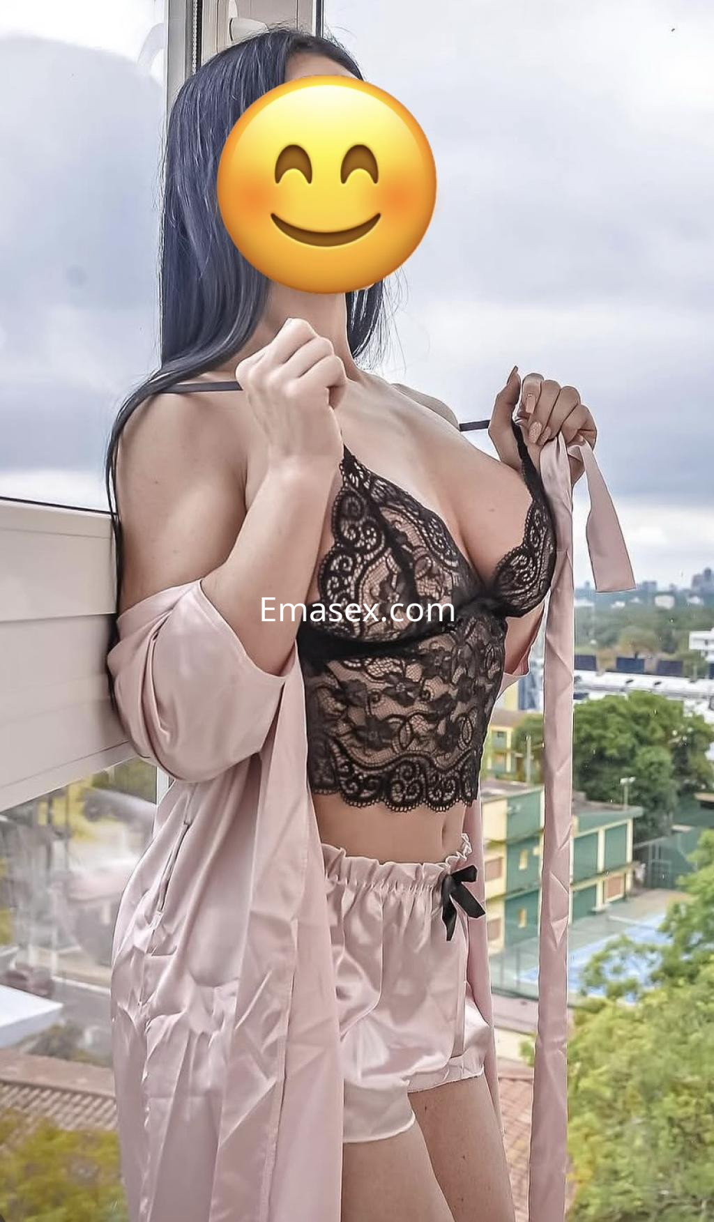 La puta luce un conjunto de lencería negra con un abrigo rosa, posando junto a una ventana en Bilbao.