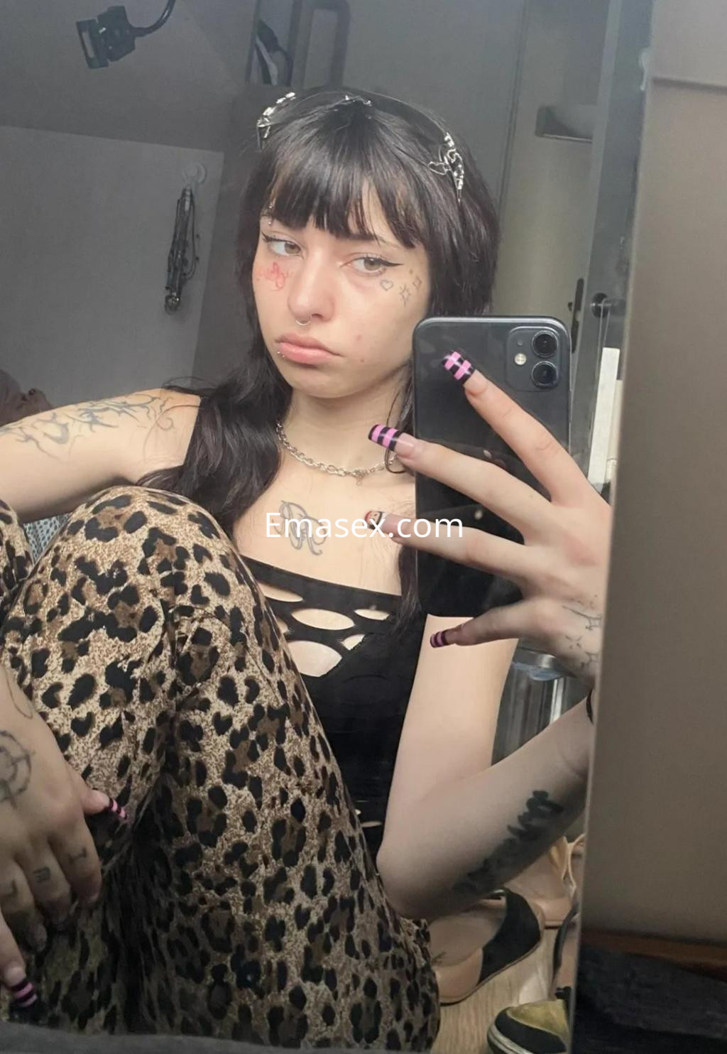 La puta en Barcelona se muestra en un espejo, luciendo un top negro, pantalones de leopardo y maquillaje distintivo.