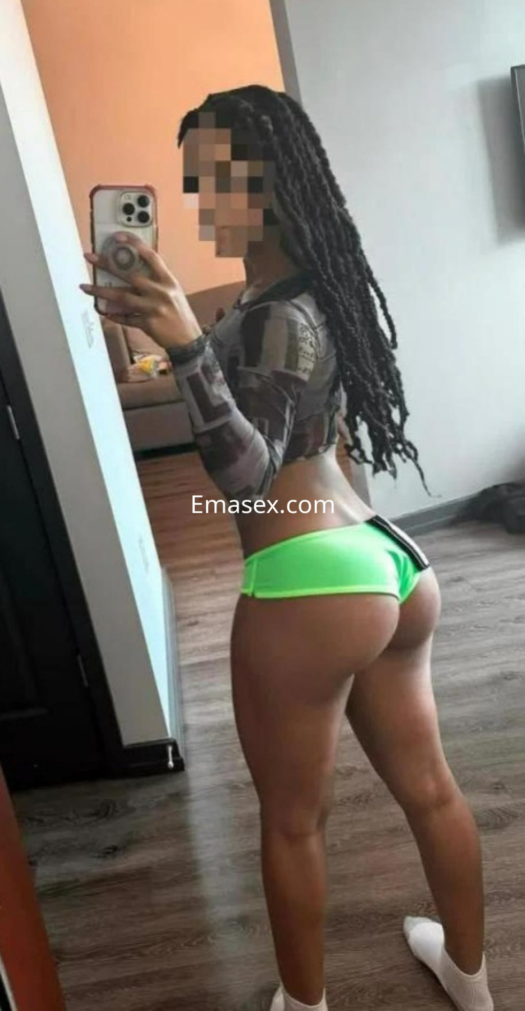 Puta de piel morena con trenzas, viste top ajustado y tanga verde, posando en un moderno ambiente interior en Madrid.