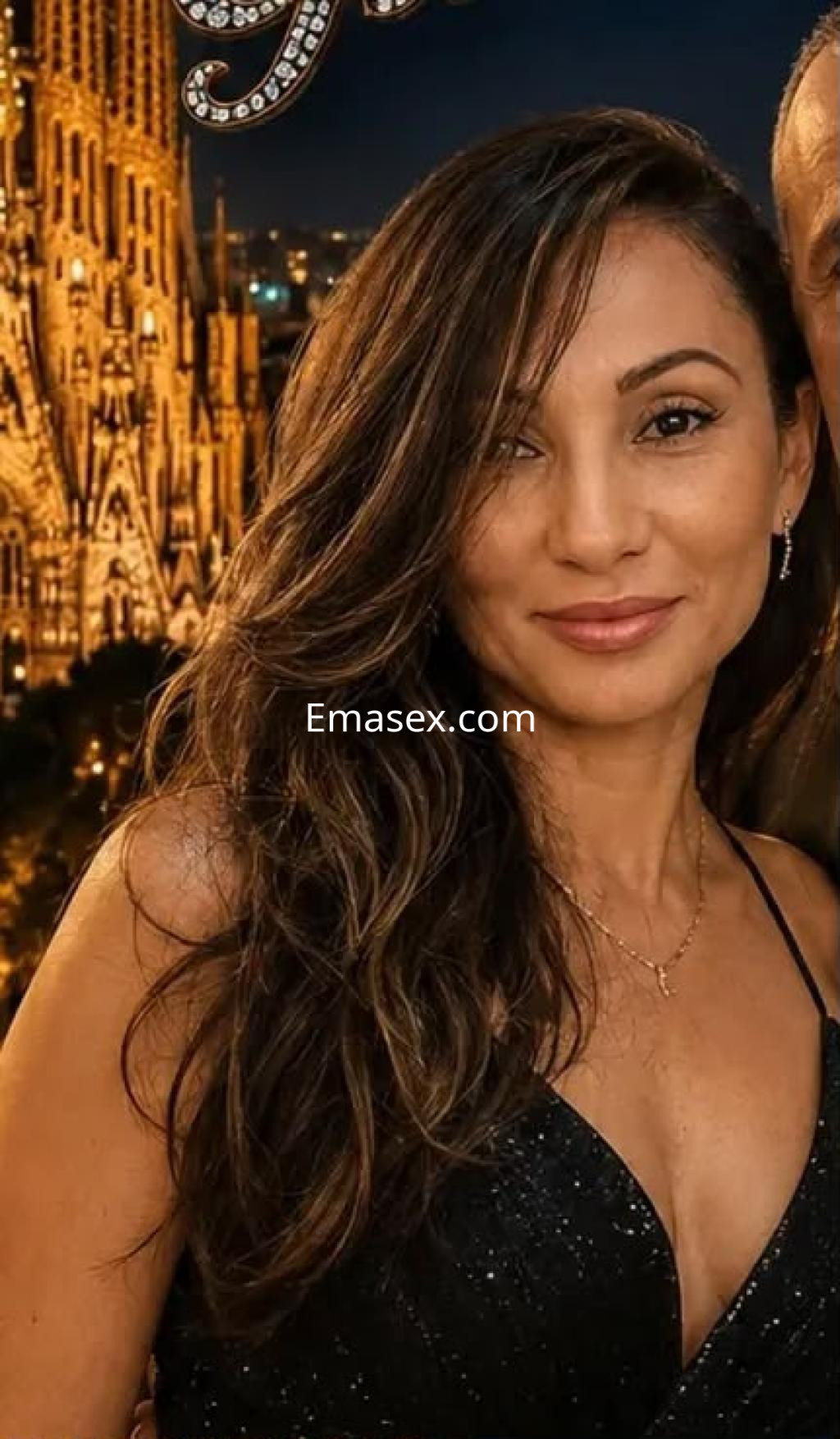Puta con cabello largo y ondulado, vestida con un top negro, sonríe frente a un fondo iluminado de Santander.