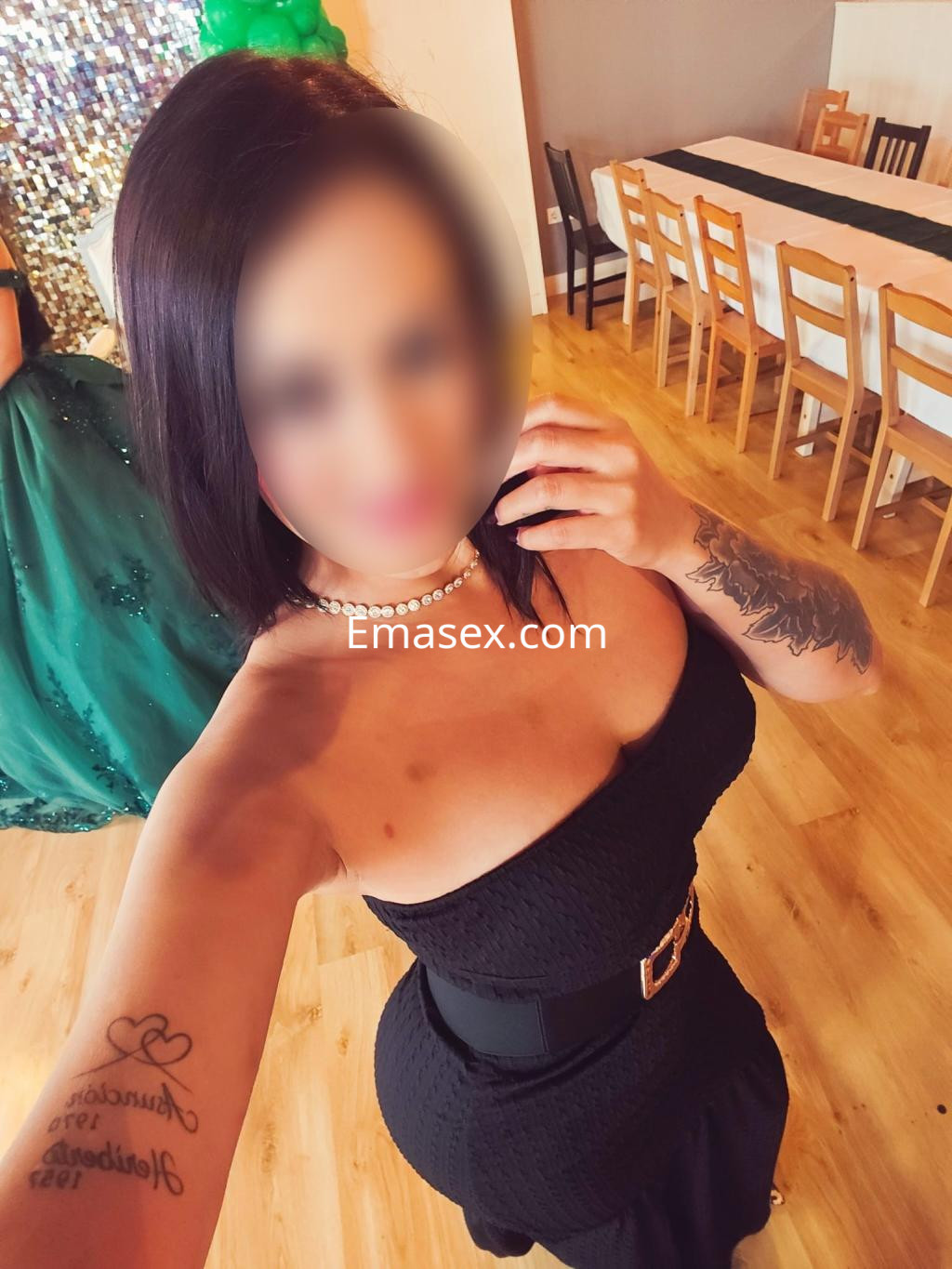Escort en Bilbao con cabello corto y oscuro, luciendo un vestido negro ceñido y collar de perlas en un ambiente festivo.