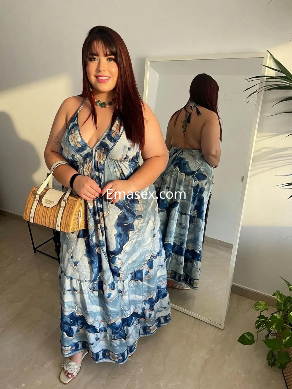 Escort en Alicante, posando frente a un espejo, lleva un vestido largo de estampado colorido y accesorios elegantes.