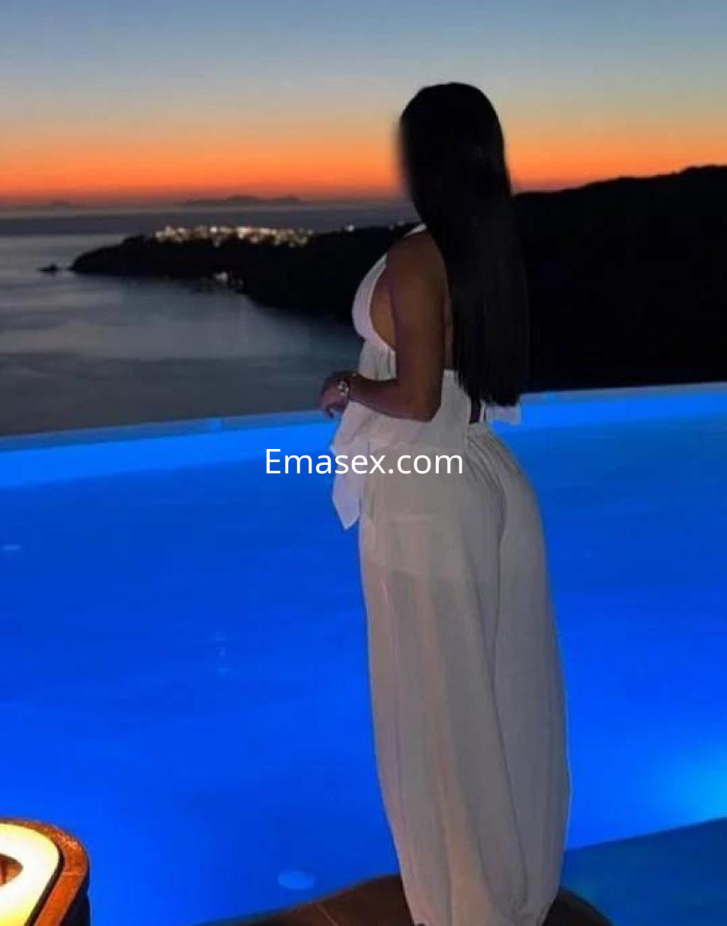 Puta de Almería, de cabello largo y oscuro, viste un conjunto blanco mientras mira el atardecer junto a una piscina.
