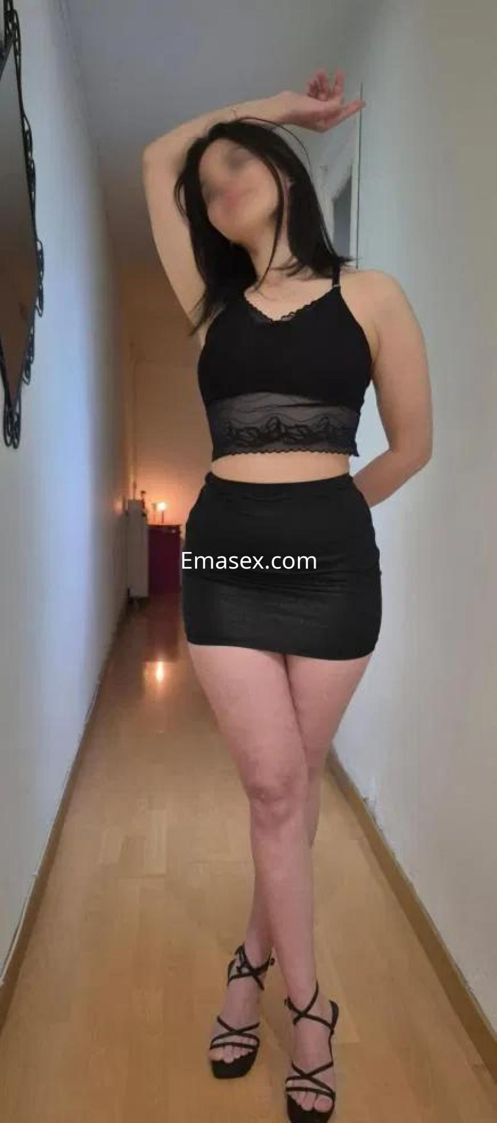 Puta posando en un pasillo, viste un top negro transparente y una falda corta, con tacones altos.