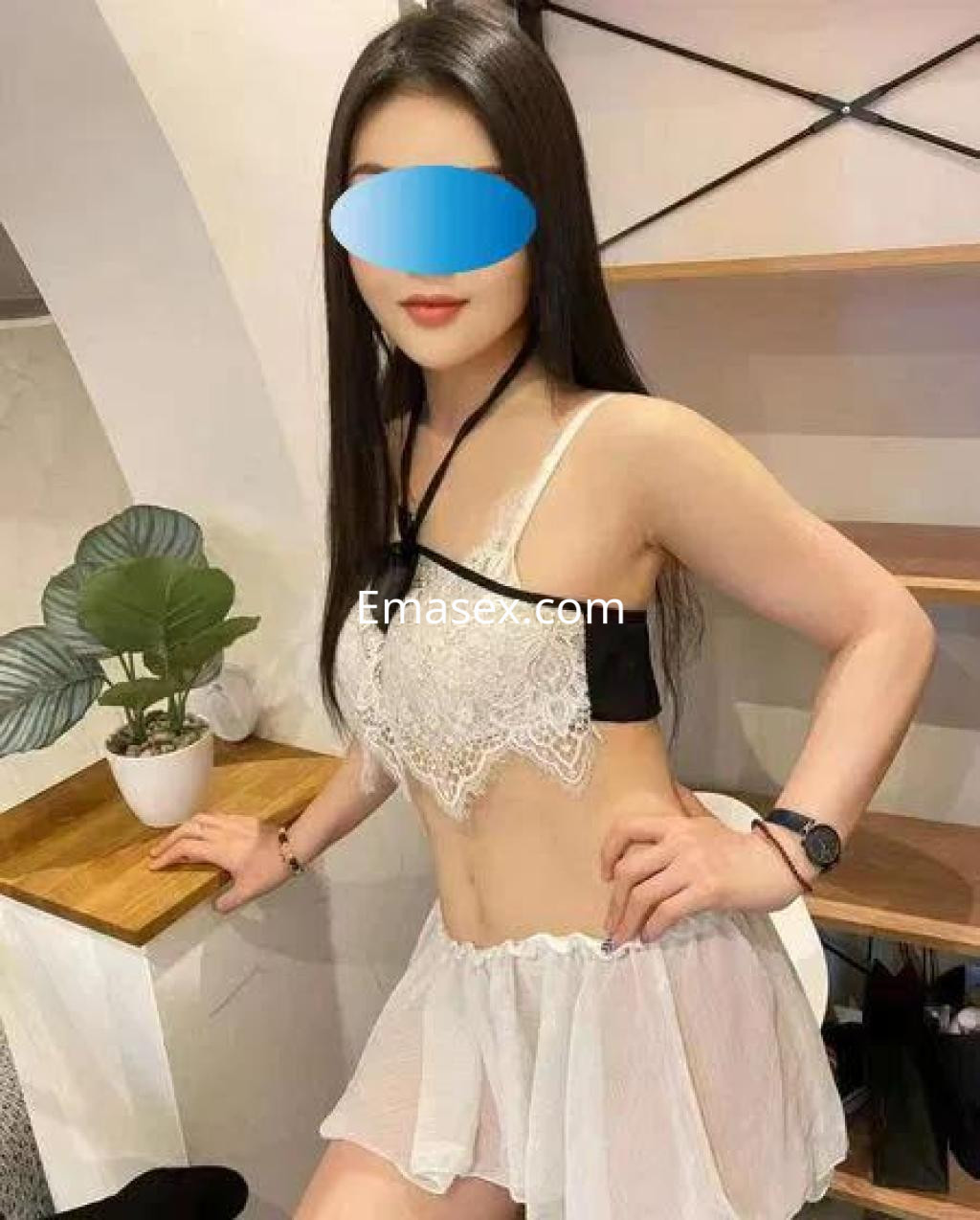 Escort en Madrid luciendo un conjunto de lencería blanca con detalles en negro, apoyada en una mesa.